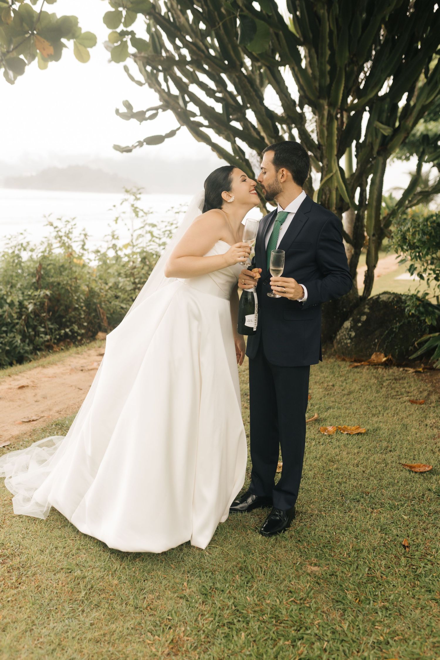 Newlyweds share a romantic kiss while holding champagne glasses at their outdoor celebration.