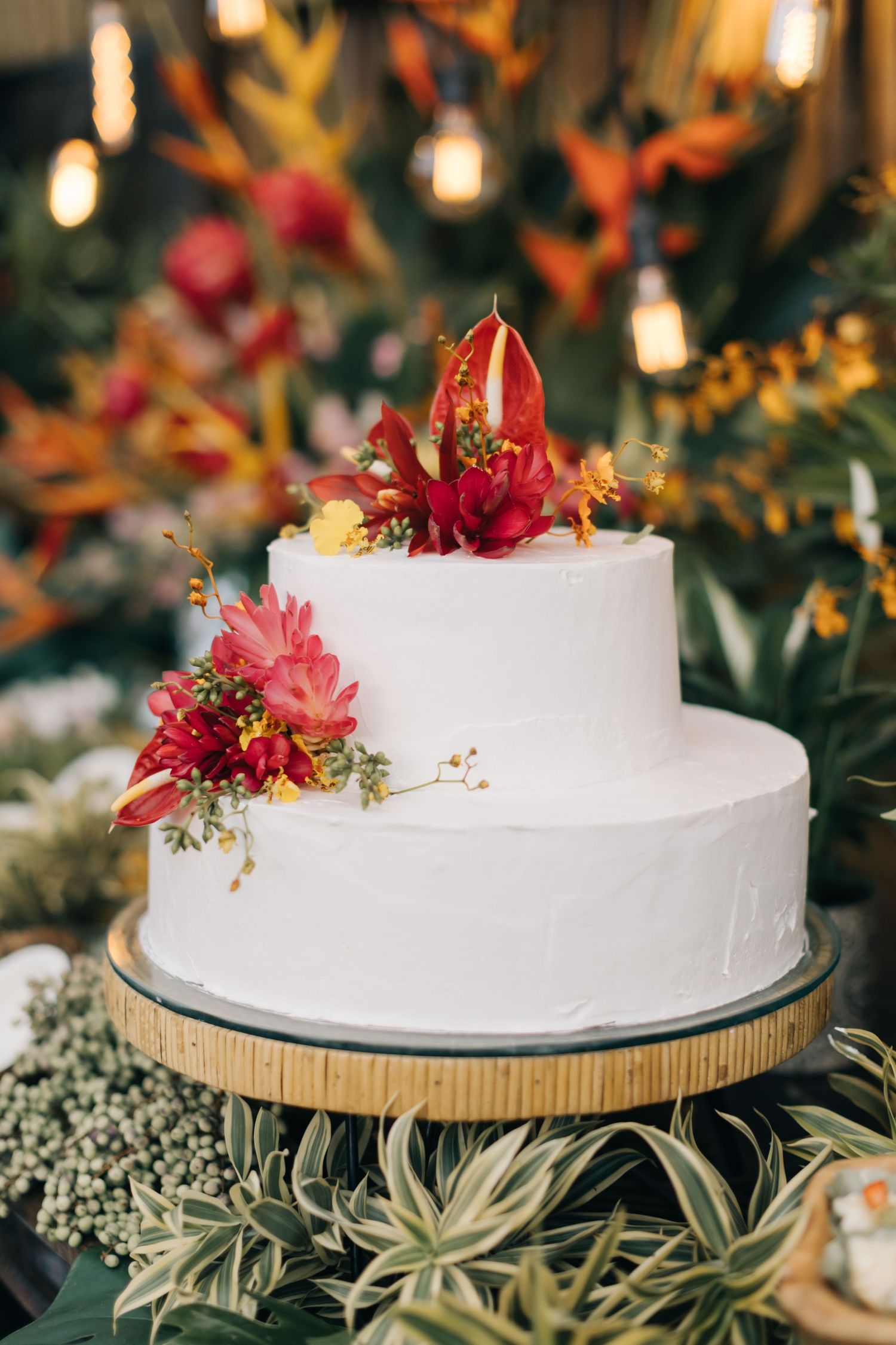 White wedding cake decorated with vibrant red tropical flowers on a golden stand.