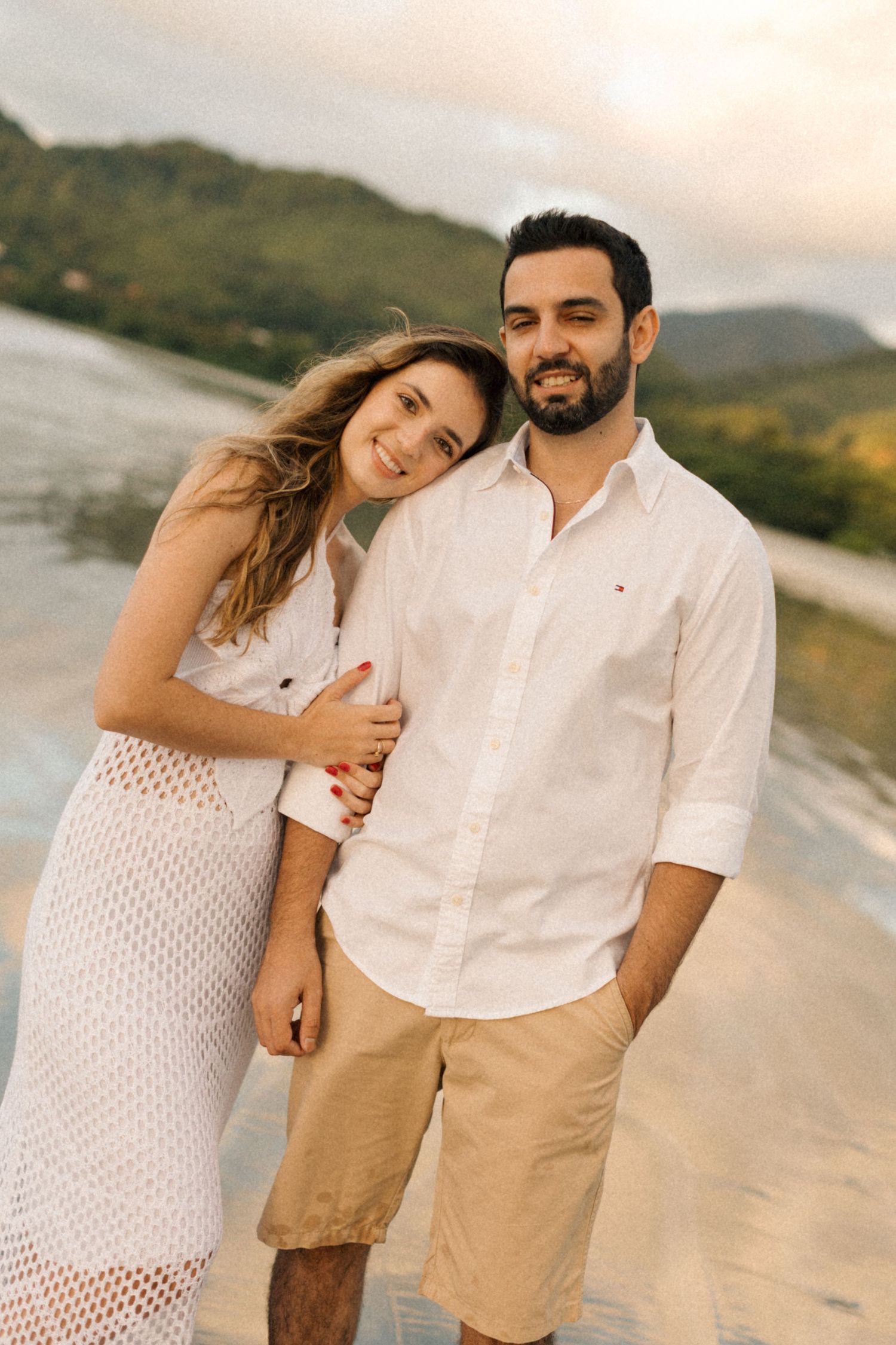 Happy couple in white and beige outfits laughing together on beach during golden hour.