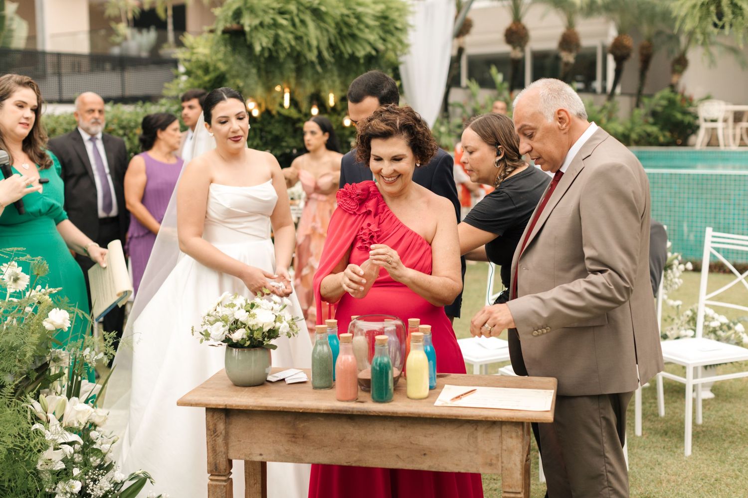 Wedding party gathered around a wooden table during an outdoor ceremony with decorative bottles.