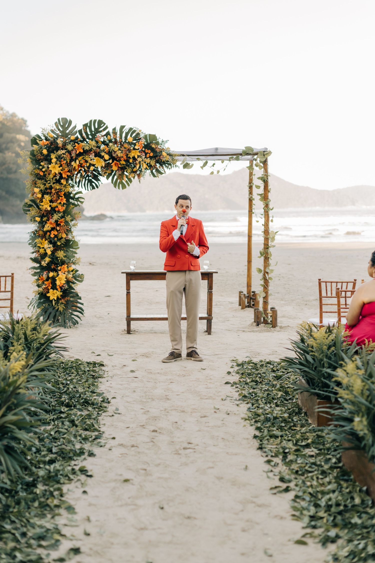 Beach wedding ceremony setup with floral arch and green aisle decor.