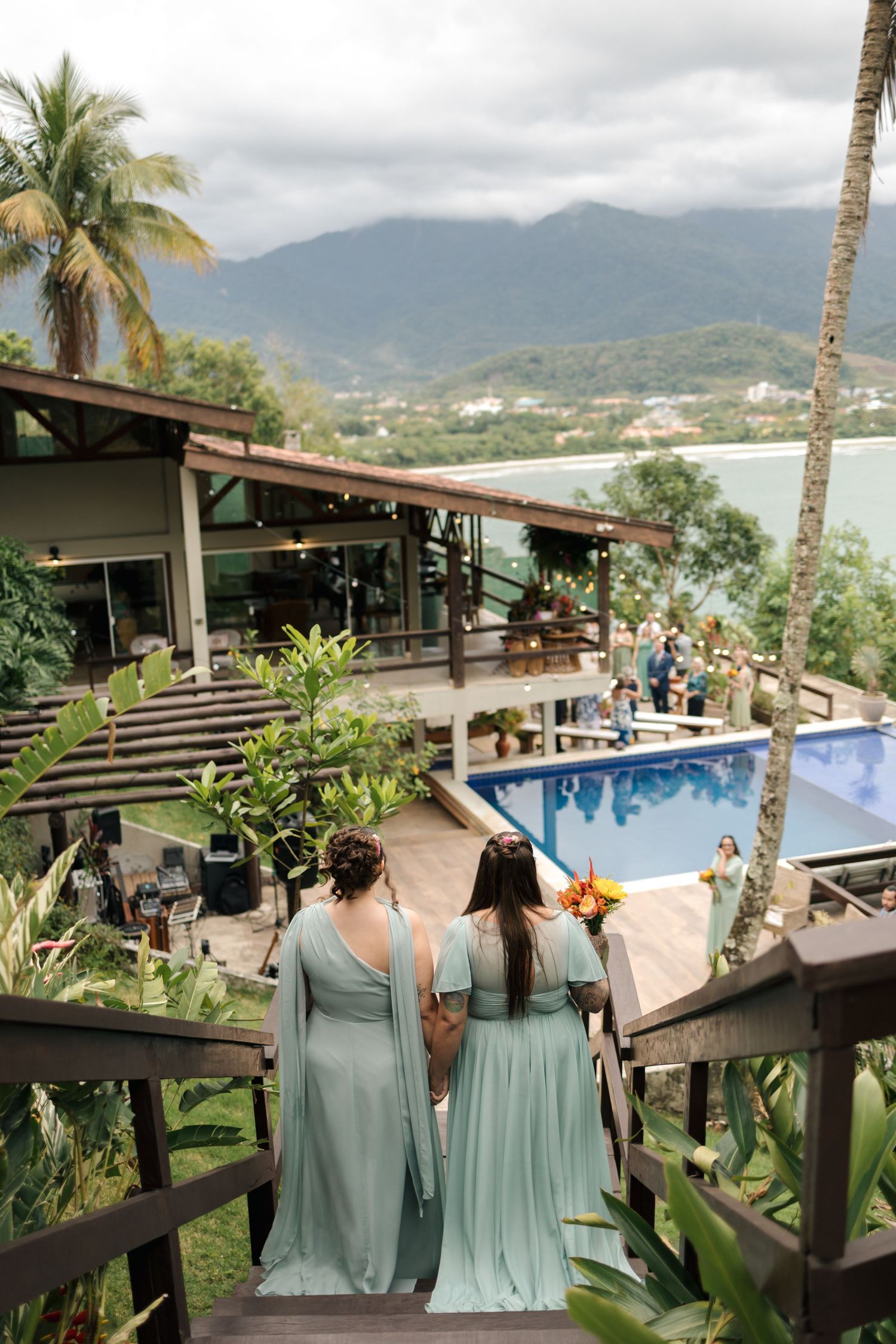 Wedding party in seafoam green dresses overlooking a mountain resort pool with palm trees.