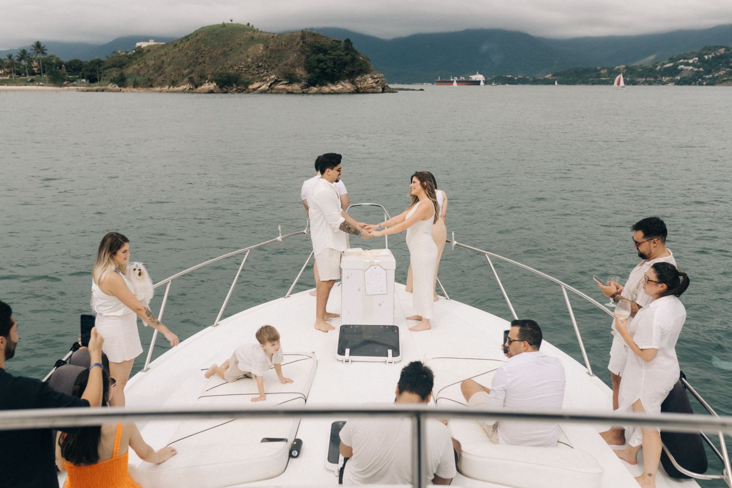 People gather on a yacht deck celebrating with mountains visible in the distance.
