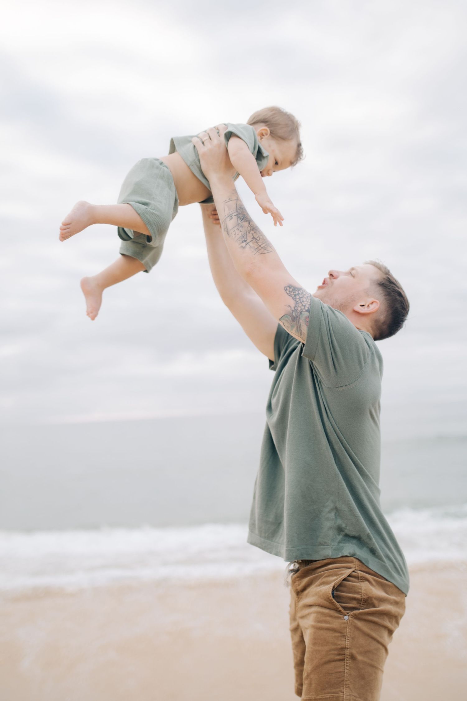 A parent lifts a toddler high in the air while playing on the beach.