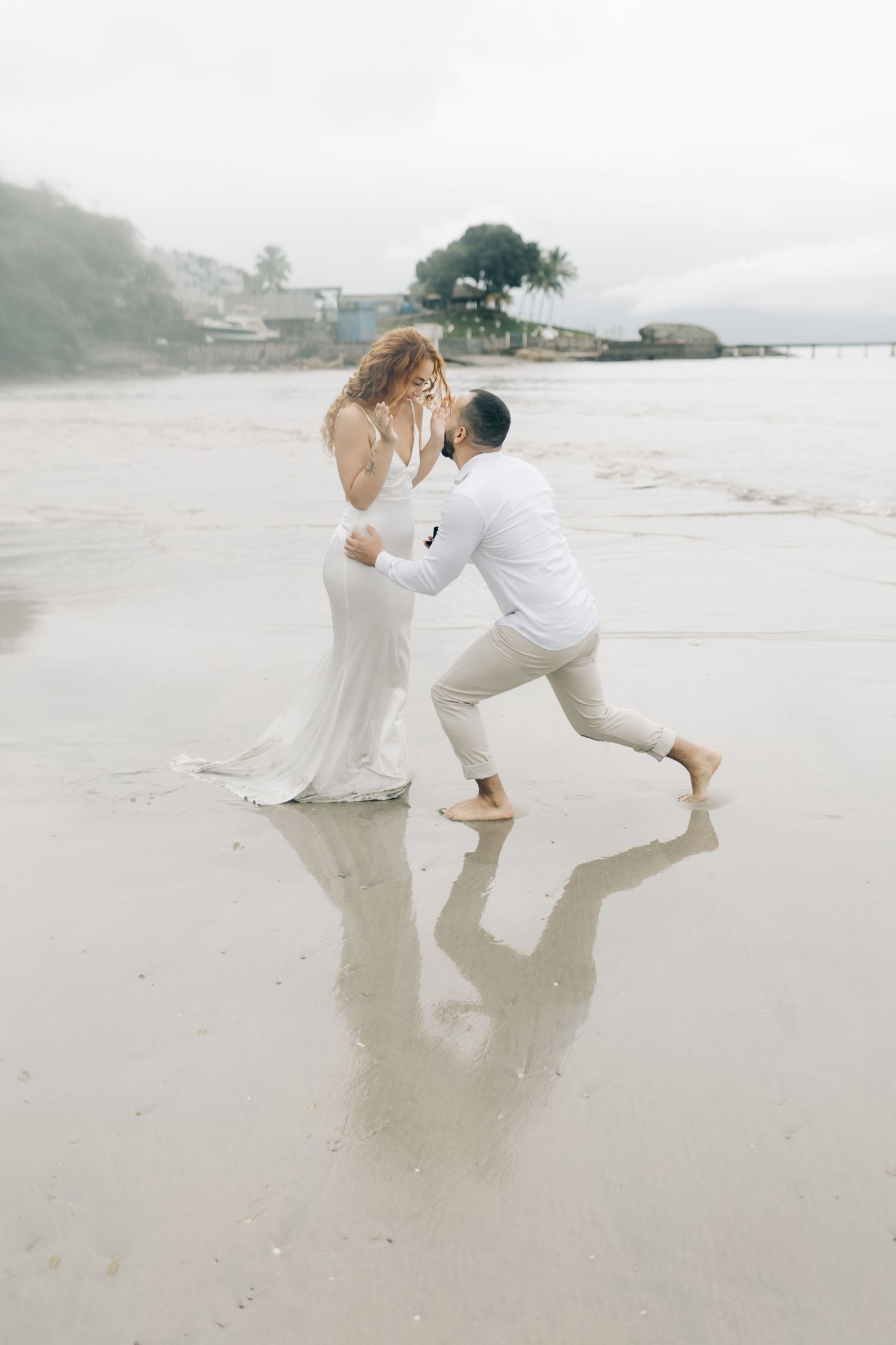 A romantic couple embraces on a misty beach, with the person in white dipping their partner in an elegant dance-like pose.