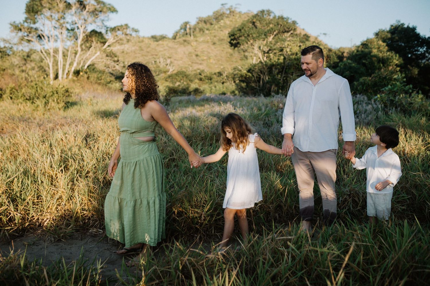 A family holds hands while walking through tall grass in a natural outdoor setting.