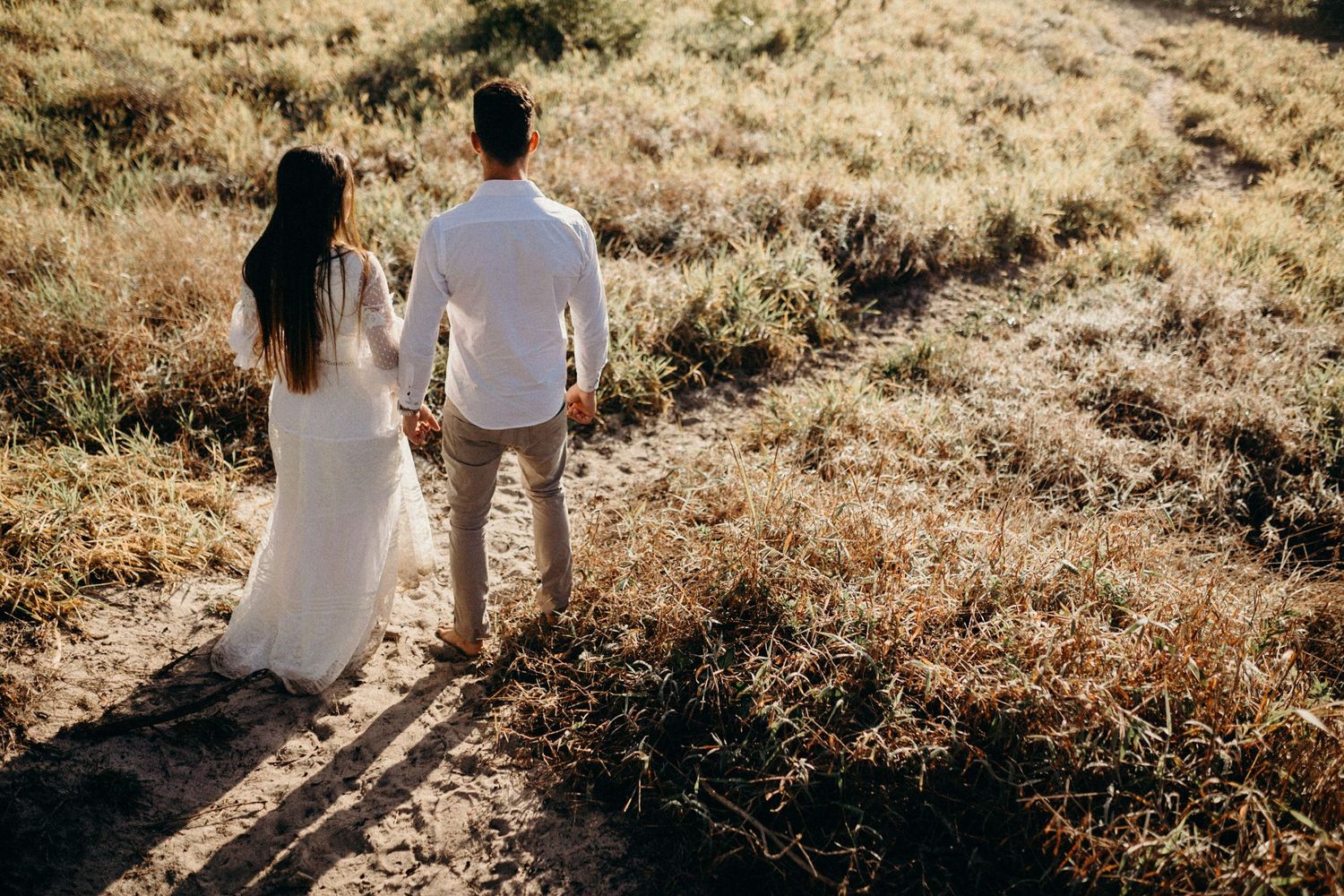 Couple holding hands while walking on hillside path during sunset.