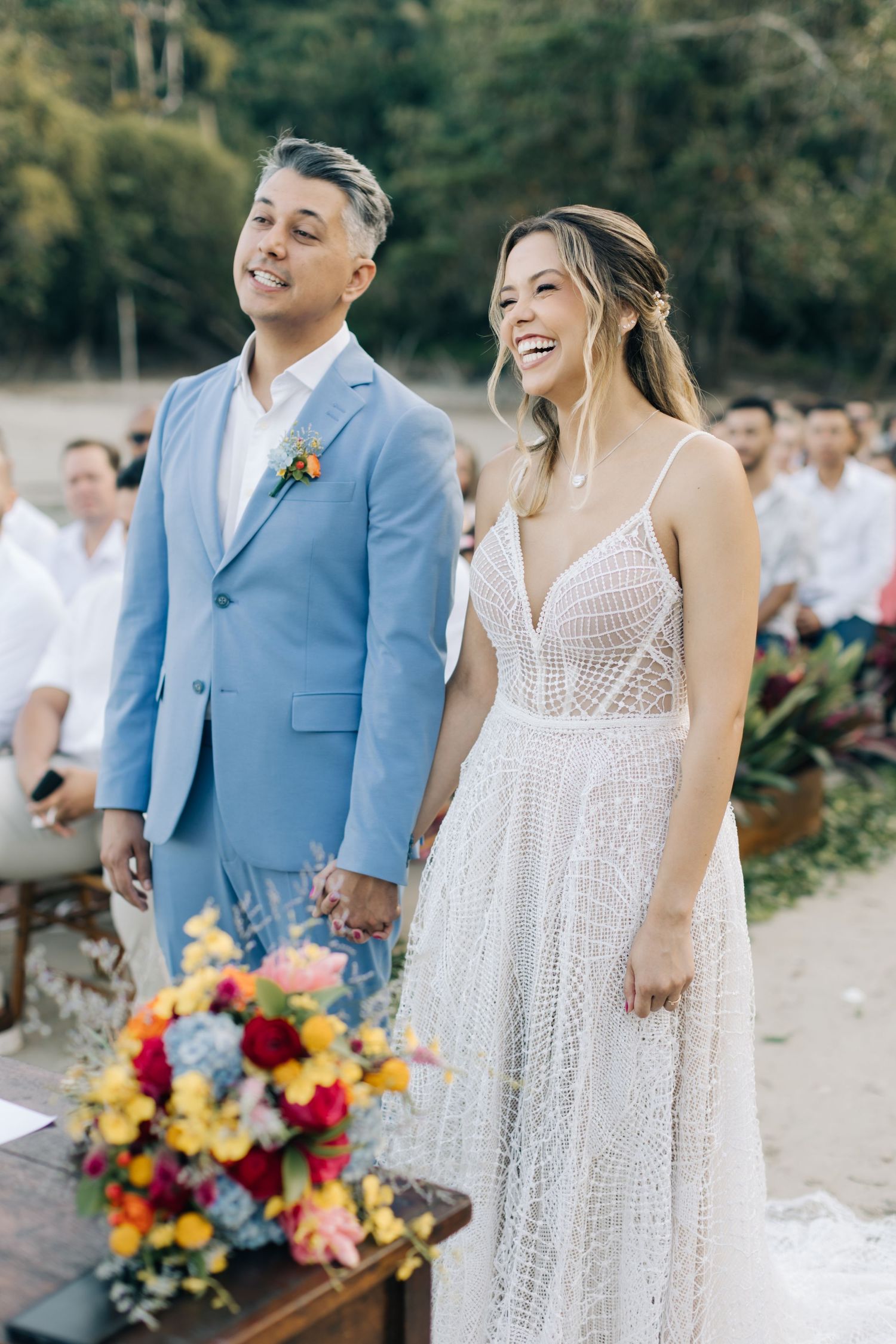A couple shares a happy moment at their beach wedding with vibrant floral bouquet.