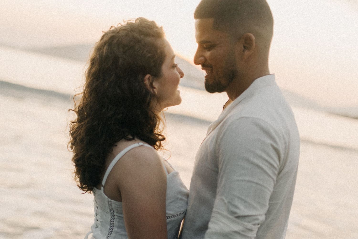 Romantic beach photoshoot with couple in white clothing at sunset.