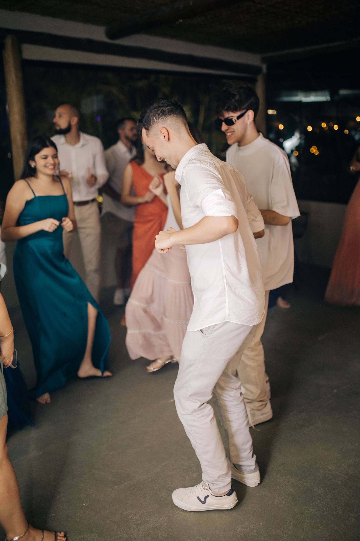 Dance party at a wedding reception with guests wearing formal attire in a dimly lit venue.