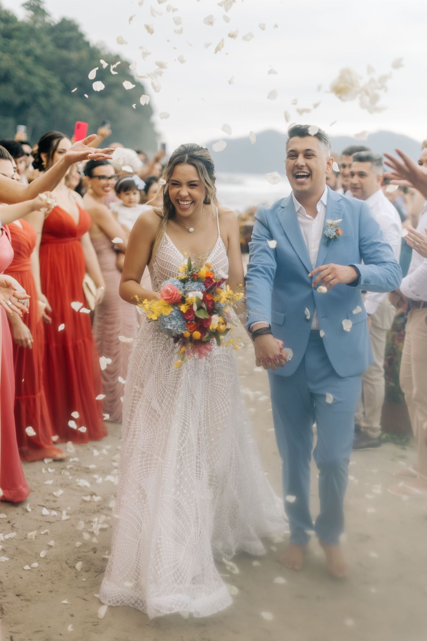 Wedding party celebrating with confetti on a beach, featuring coral and white attire.