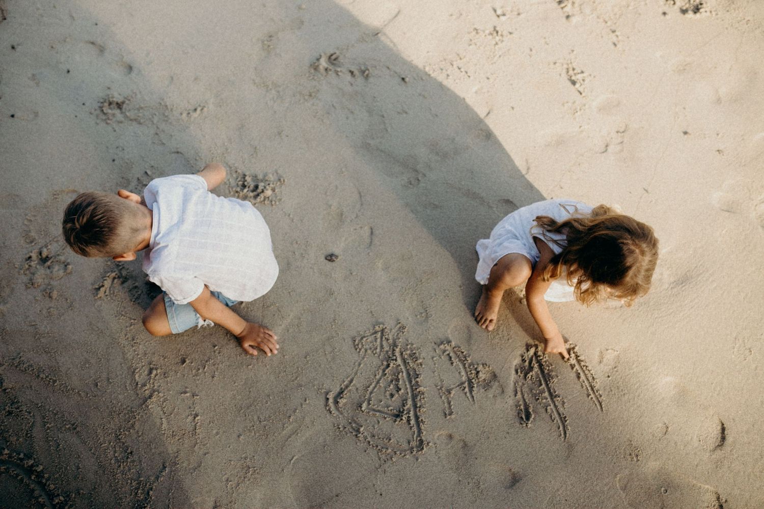 Aerial view of people drawing in beach sand from above during sunset.