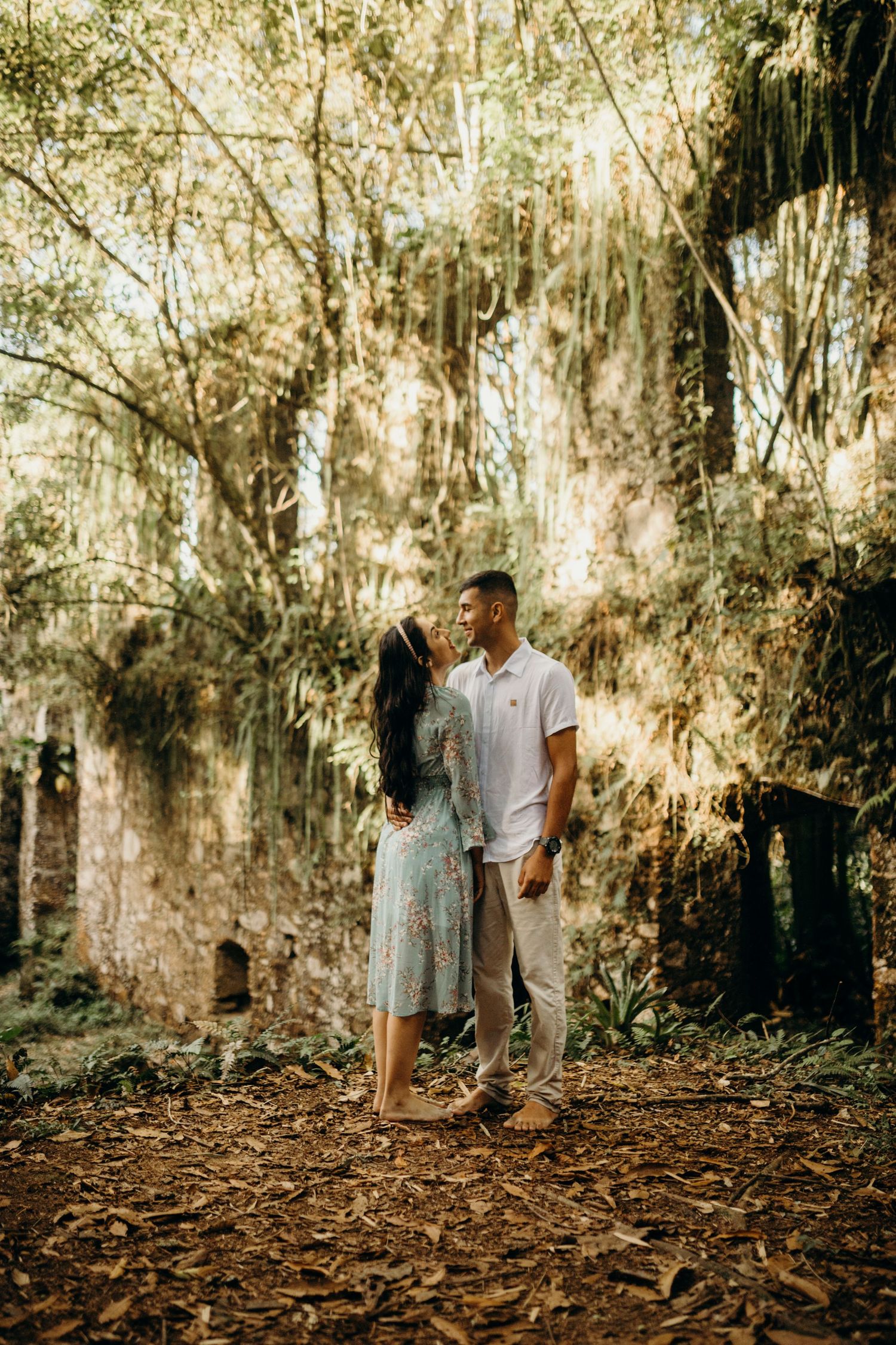 Couple standing together among ruins with Spanish moss hanging from trees in the background.