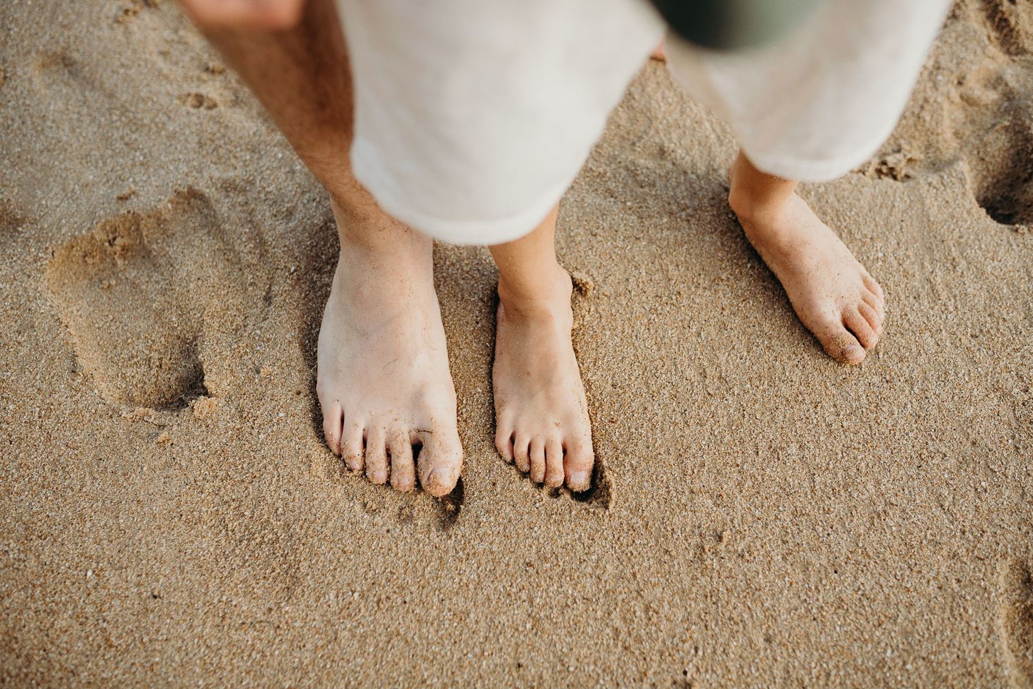 Bare feet standing in soft beach sand on a sunny day.