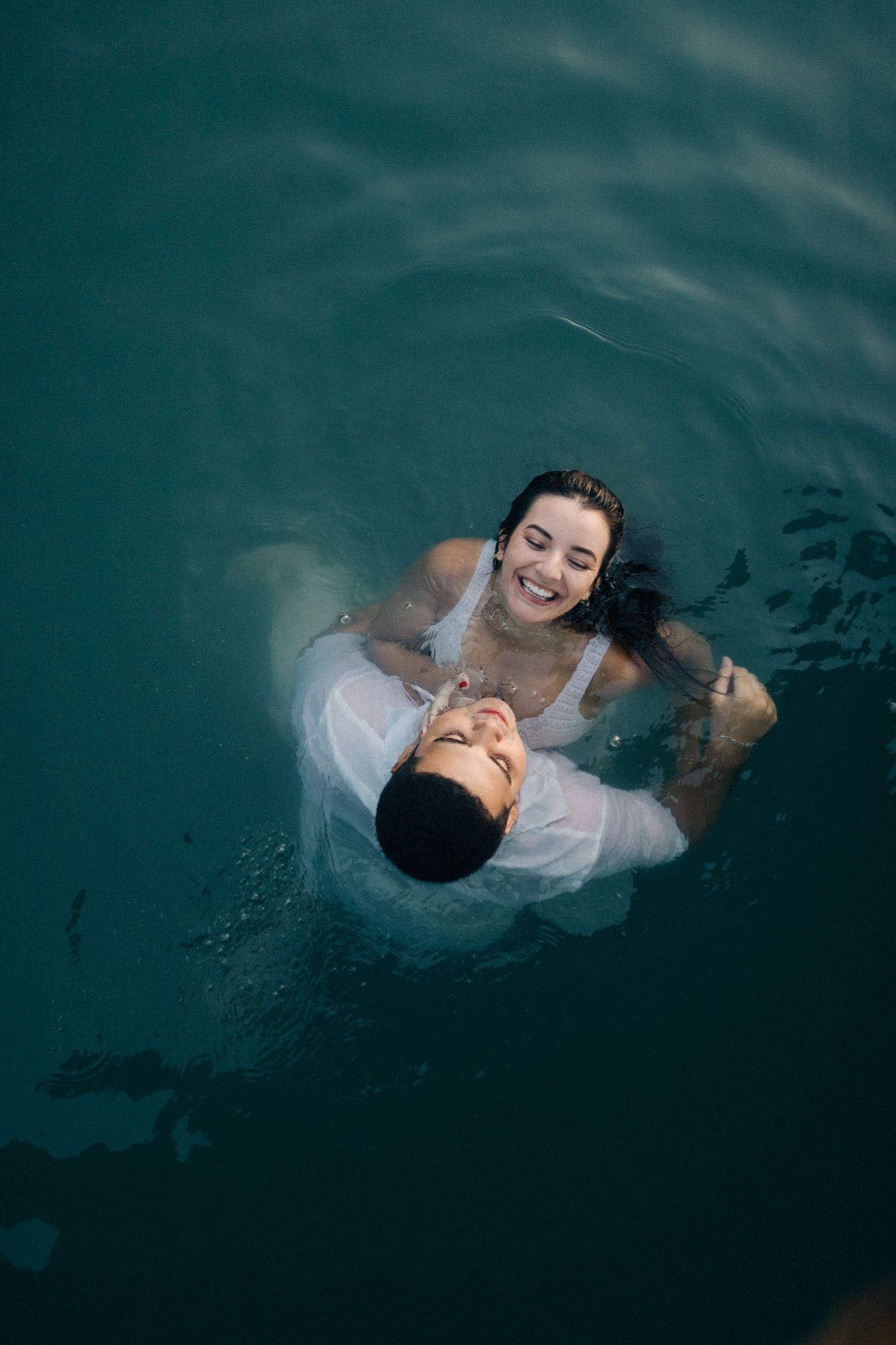 A couple floats together in deep turquoise waters during an intimate photoshoot.