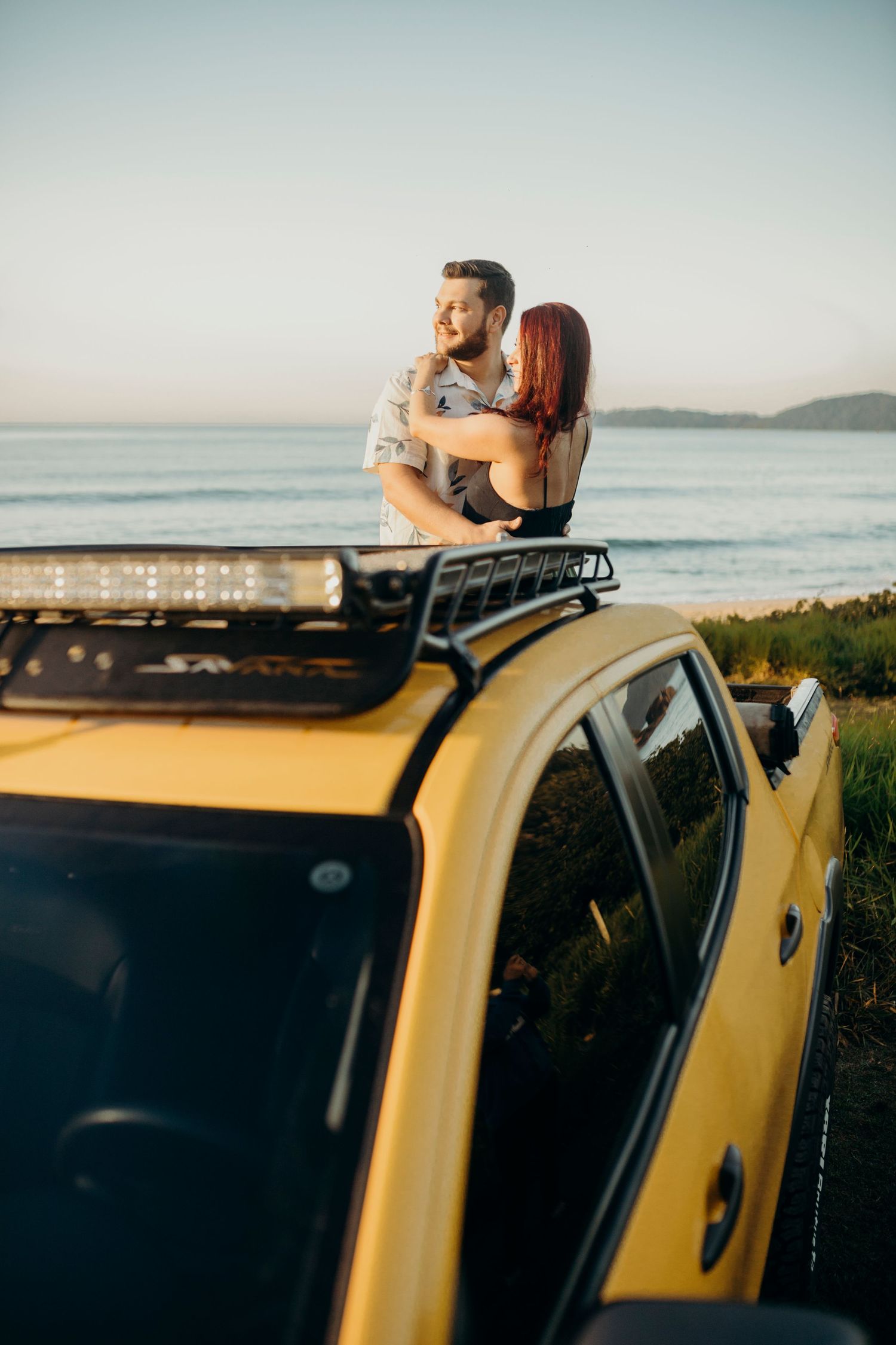 Romantic embrace on yellow pickup truck overlooking coastal sunset view.
