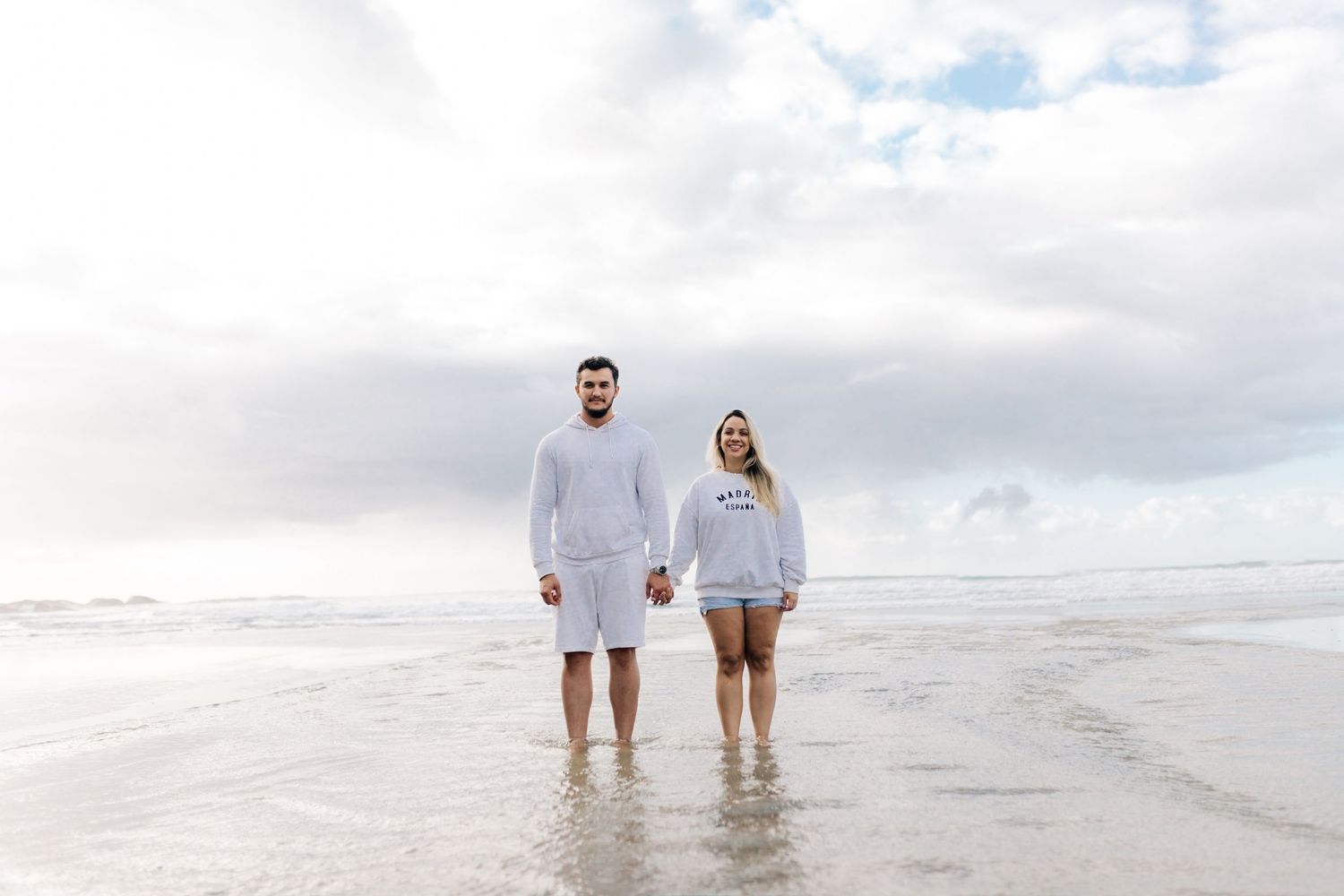 Couple wearing matching white outfits standing together on a misty beach.