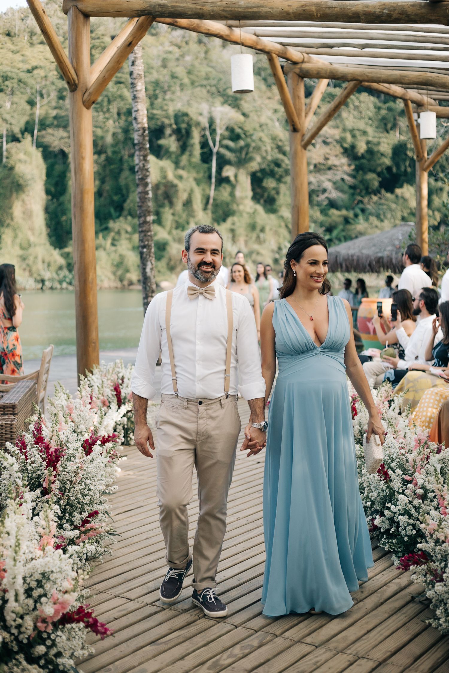 Wedding party members walking down a flower-lined wooden deck pathway.