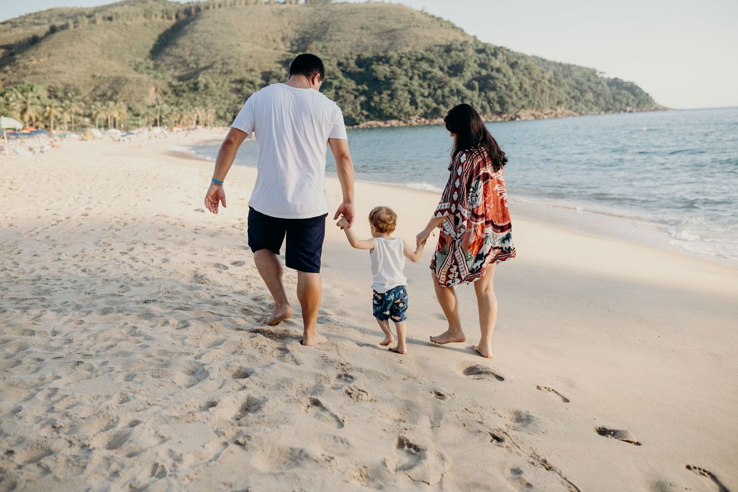 Family walking together on a sandy beach with mountainous coastline in the background.