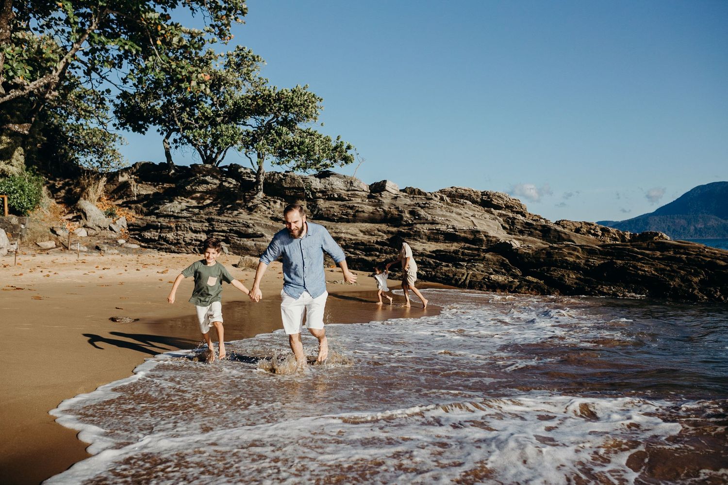 People enjoying a sunny day walking along rocky coastline with waves crashing.