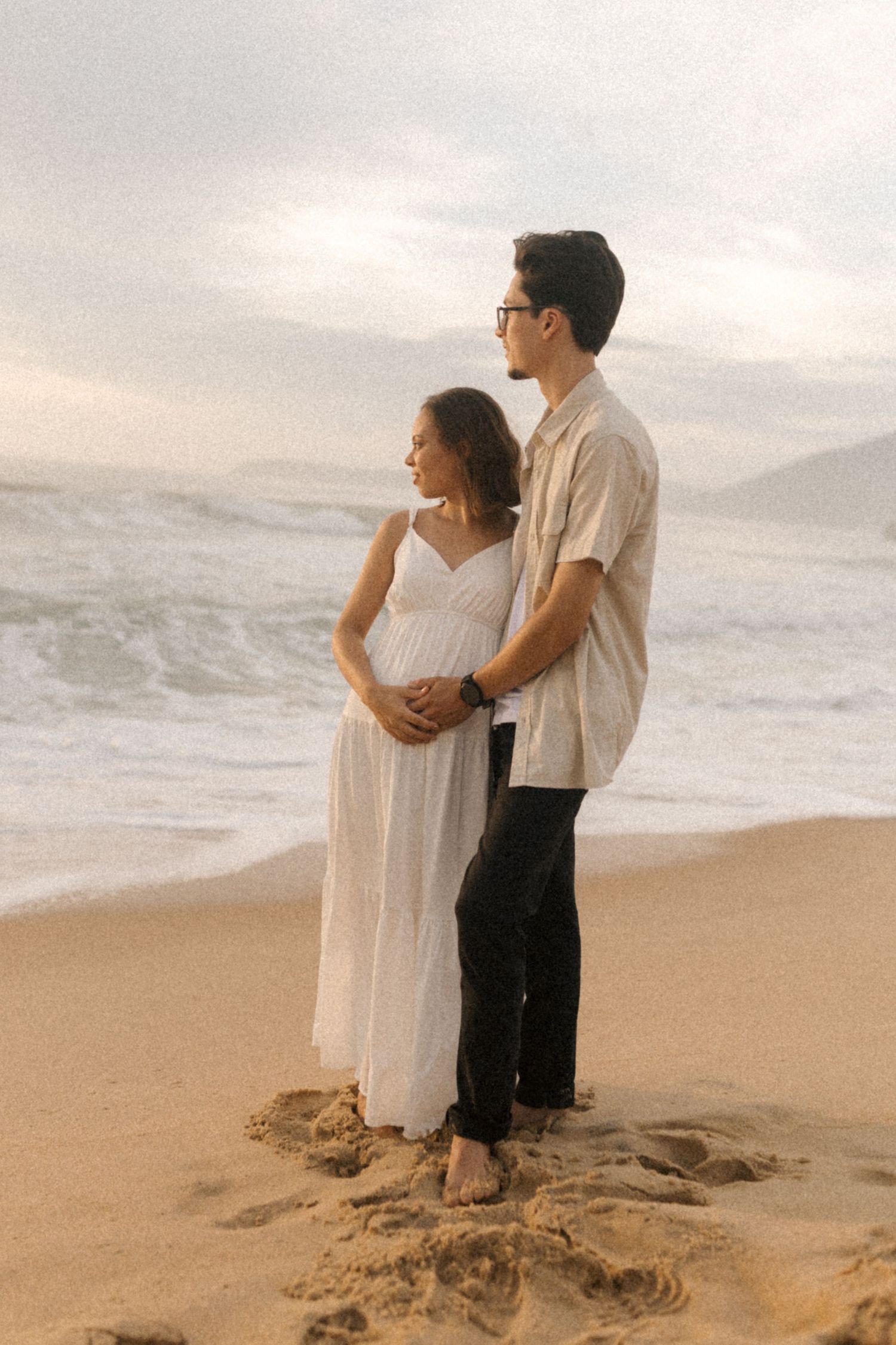 Couple embracing on beach during golden hour with waves crashing behind them.