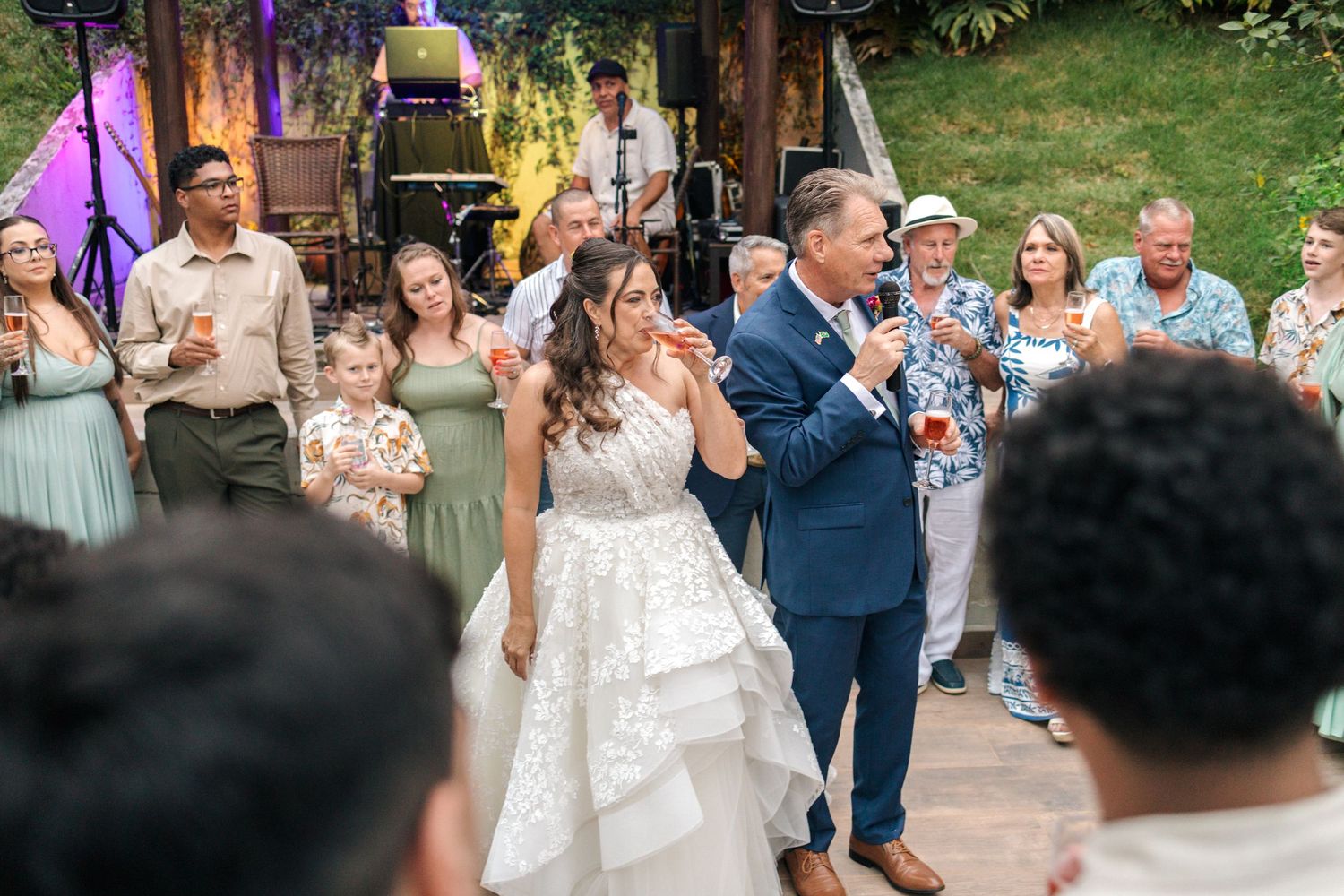 Wedding party dancing and celebrating at outdoor reception with colorful lighting.