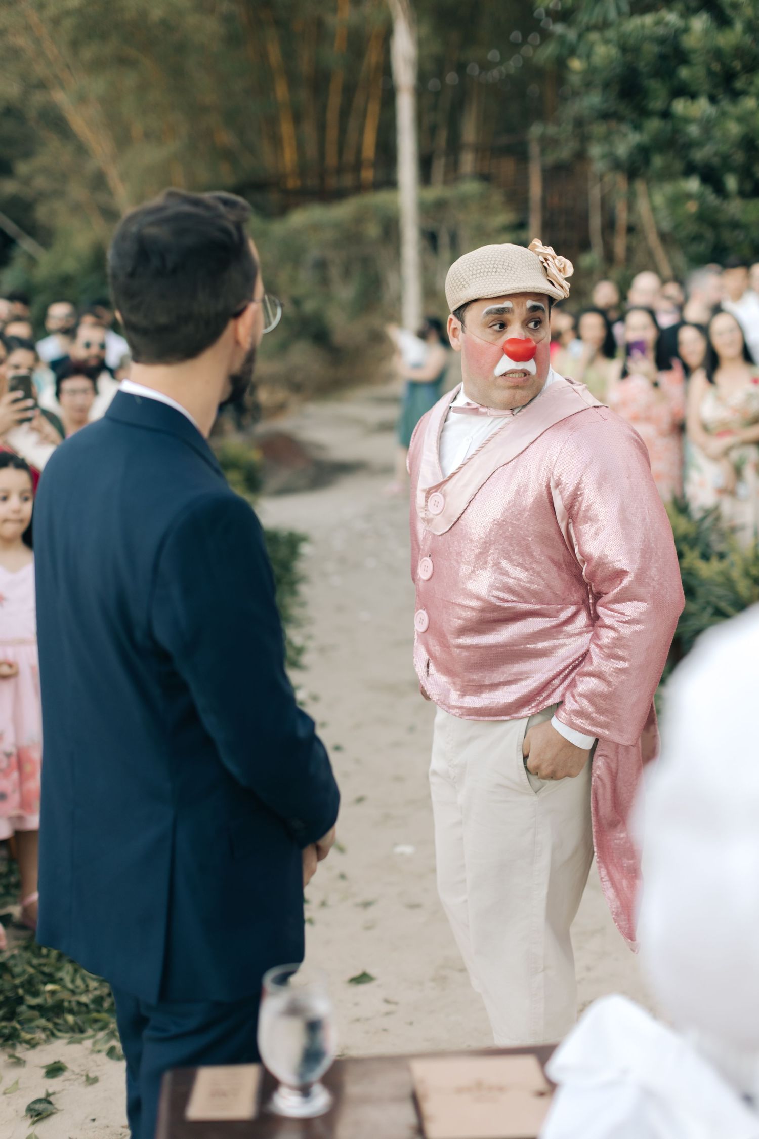 Performer in pink jacket and clown nose interacts with guest at outdoor celebration.