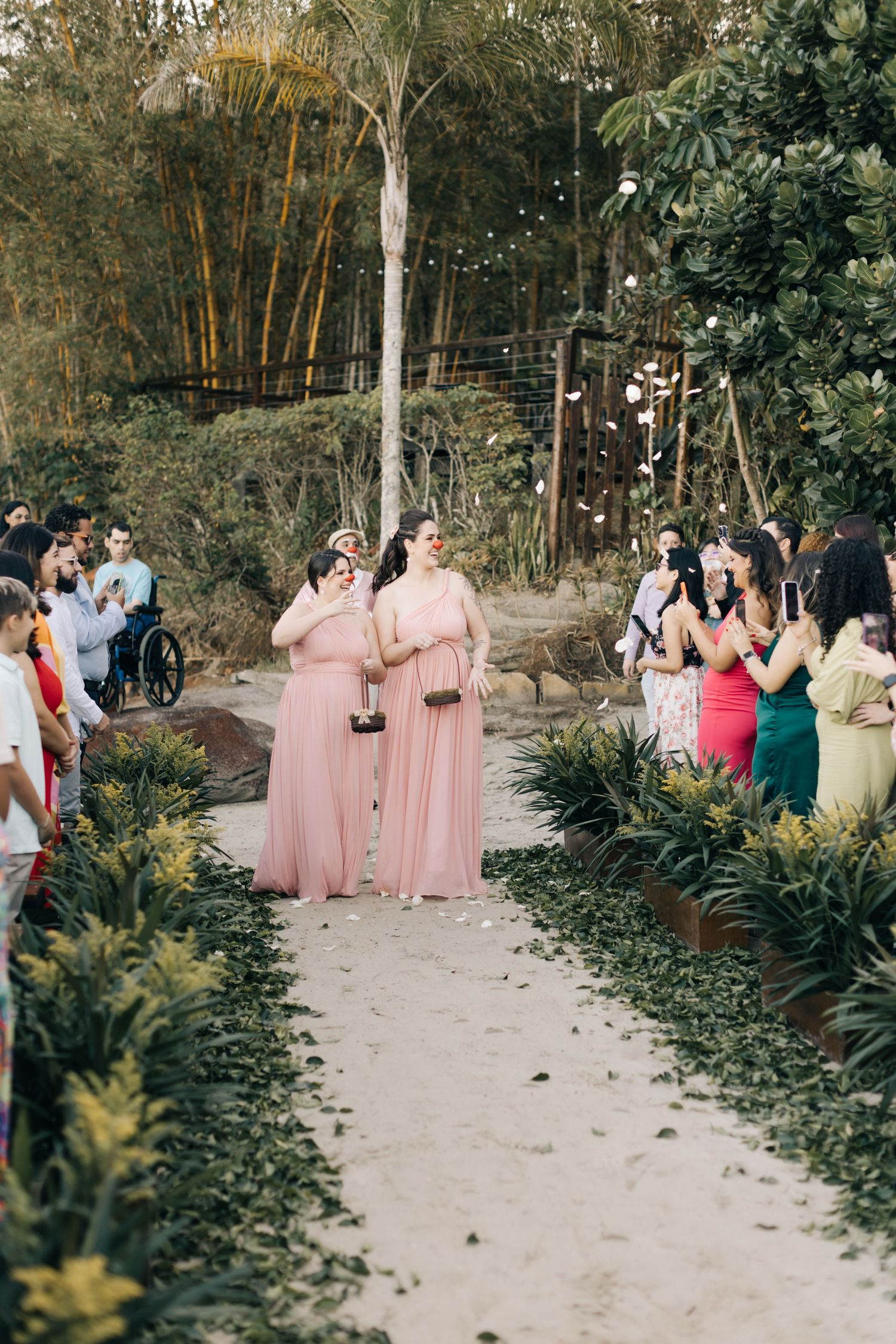 Wedding guests in pink bridesmaid dresses gather along a garden path during outdoor ceremony.