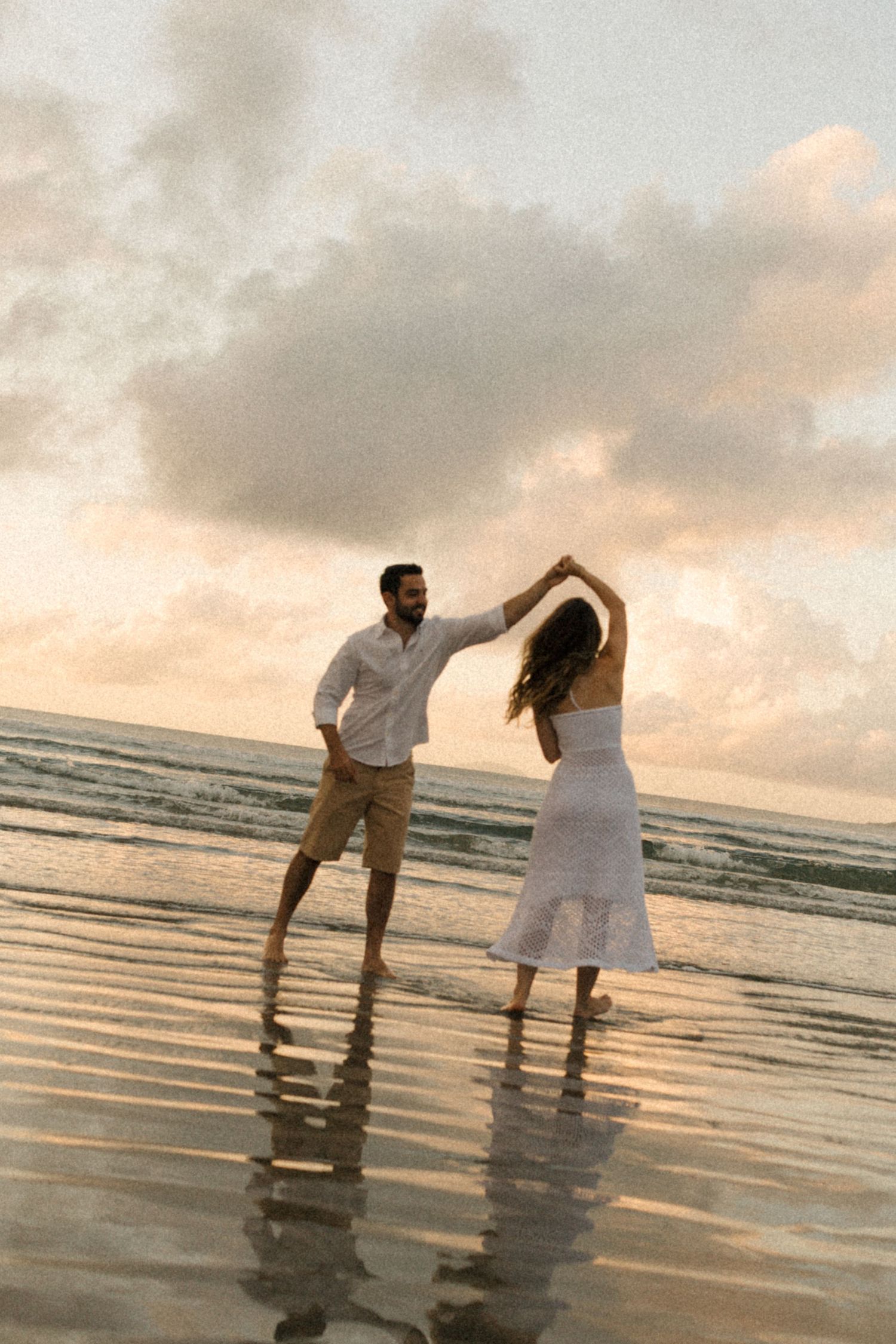 A couple dances playfully in the shallow waters of a beach at sunset.
