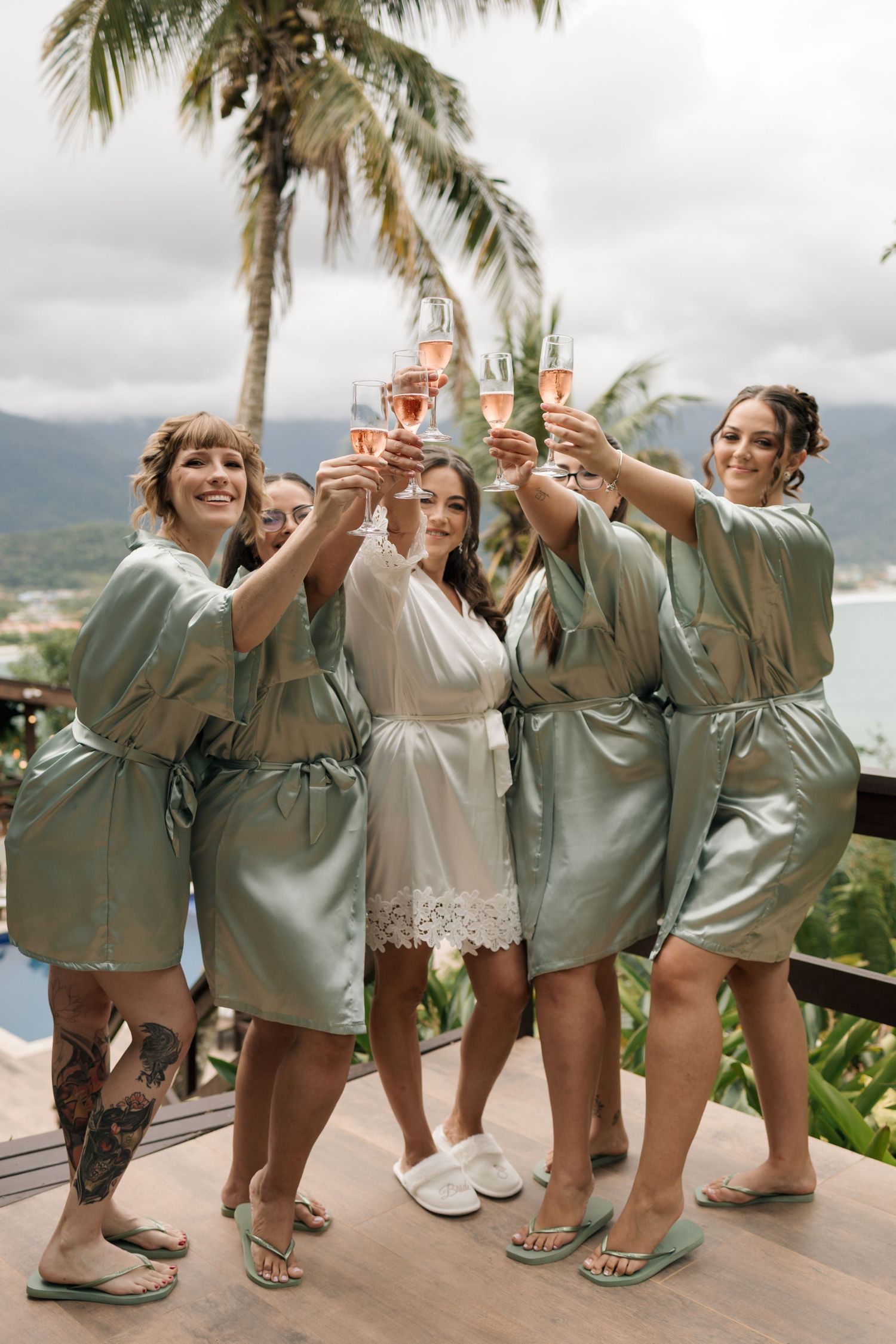 A group wearing matching robes celebrates on a tropical balcony with palm trees and ocean views.