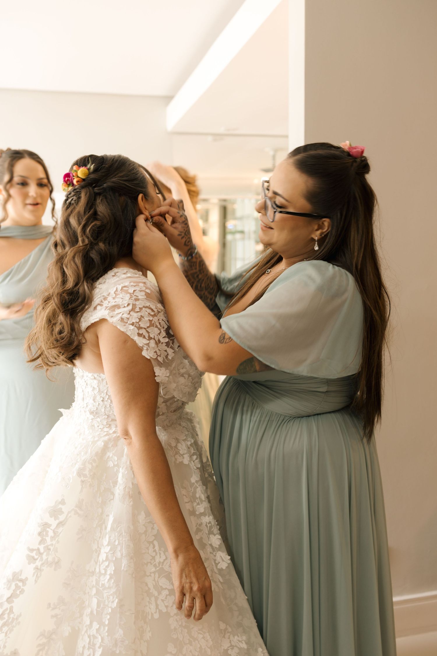 A tender moment during wedding preparations as attendants help adjust the bridal gown.