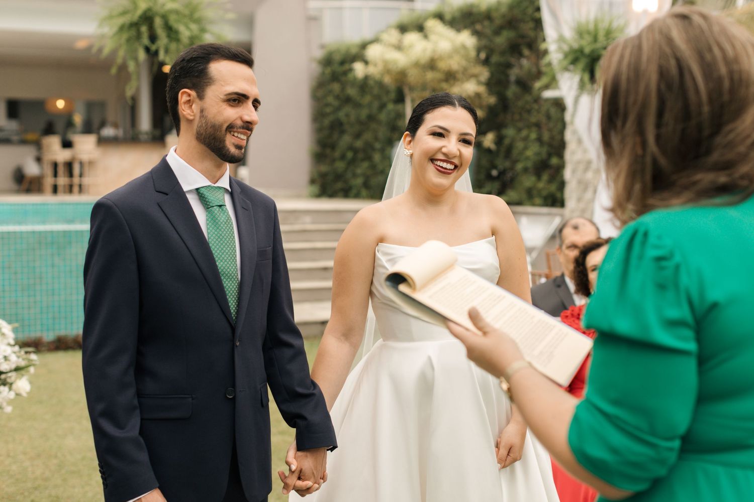 Wedding ceremony with officiant in green speaking to couple in garden setting.