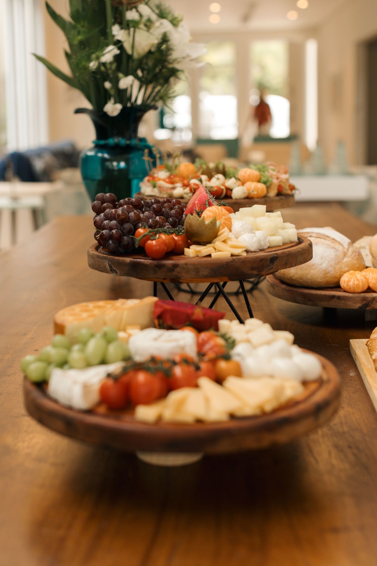 Multiple wooden platters display assorted cheeses, fruits, and appetizers on a dark table.