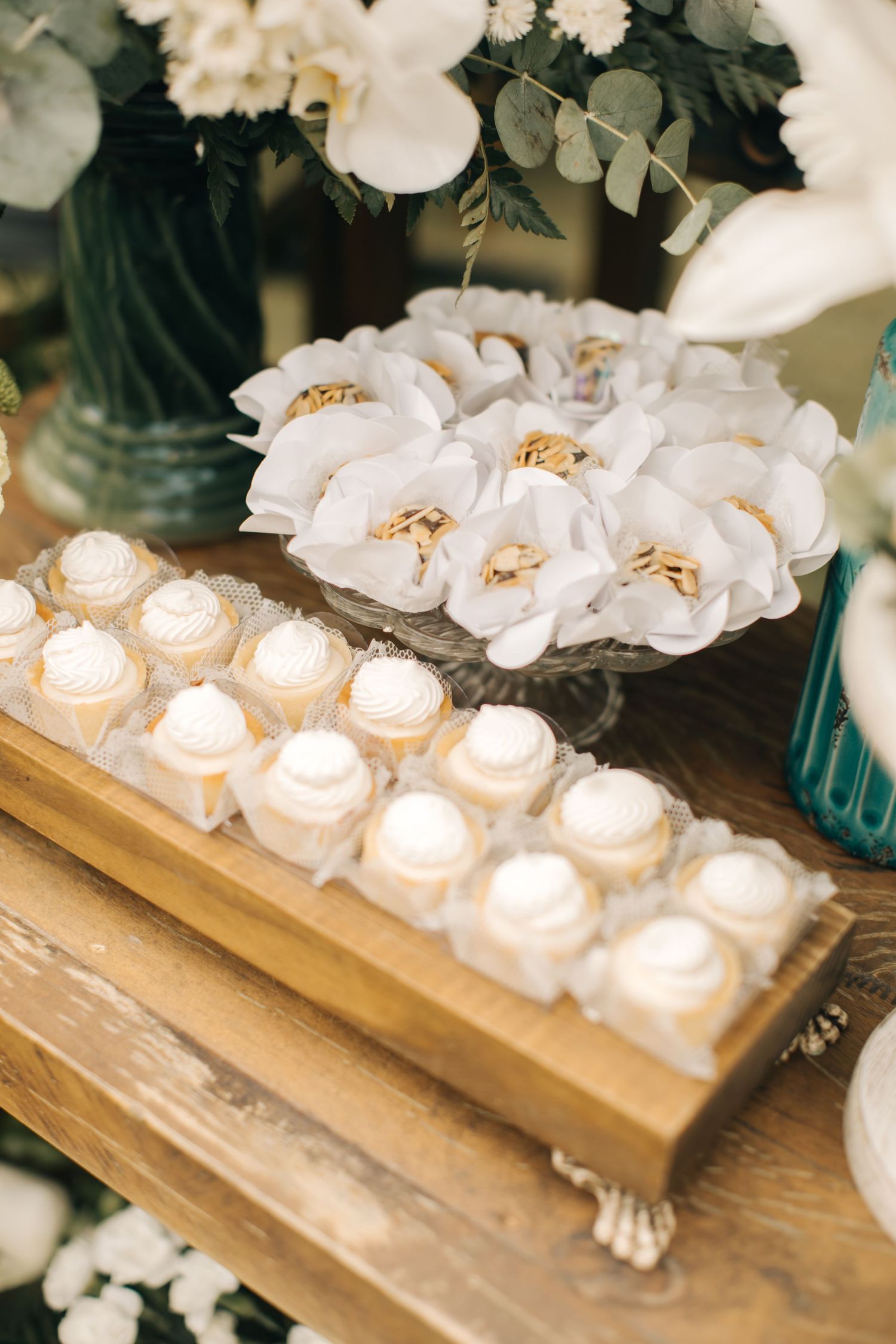 White roses and small desserts elegantly displayed on wooden table with turquoise accents.