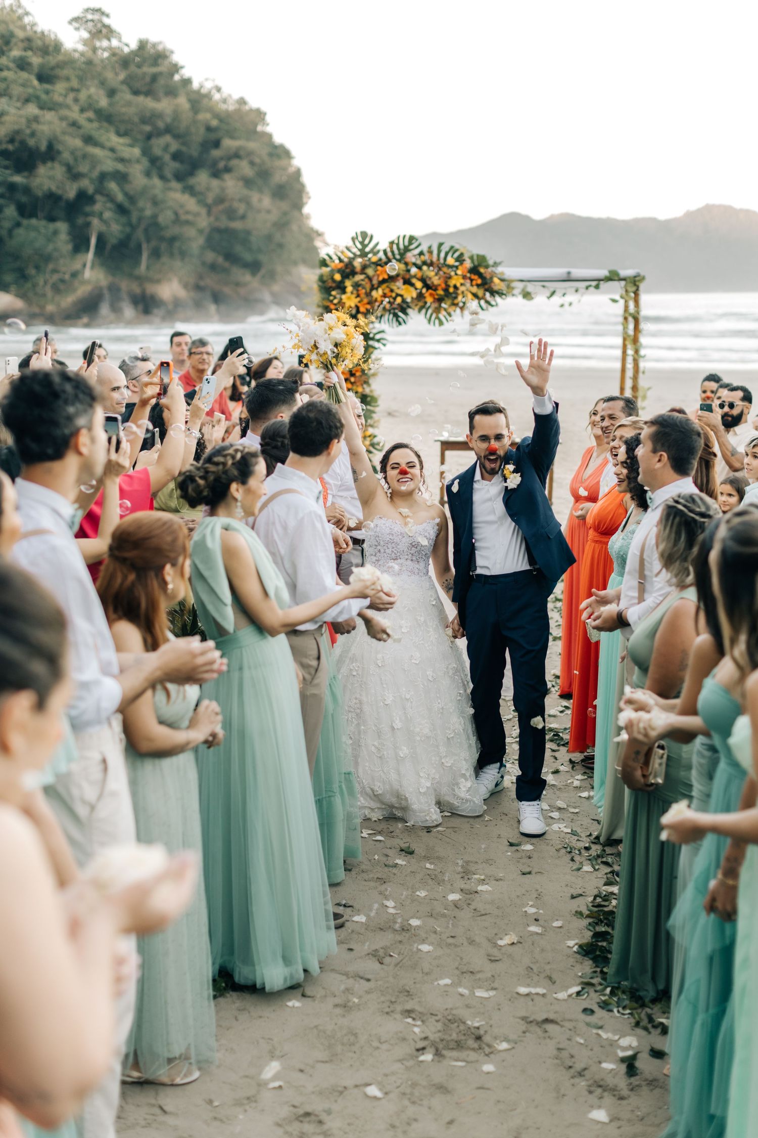 Wedding guests in mint green dresses line beach pathway during celebration.