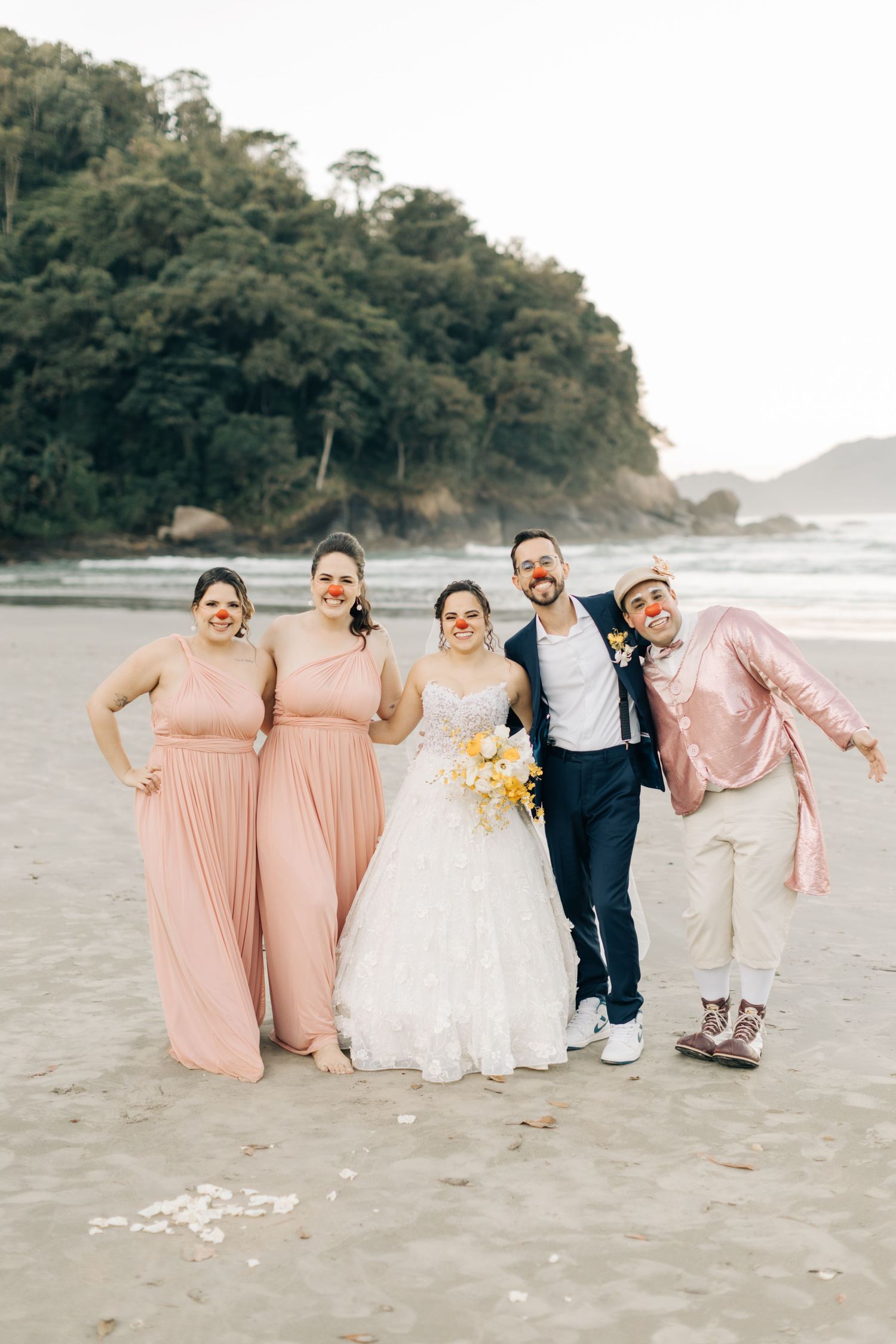 Bridal party poses playfully on beach in pink and white attire.