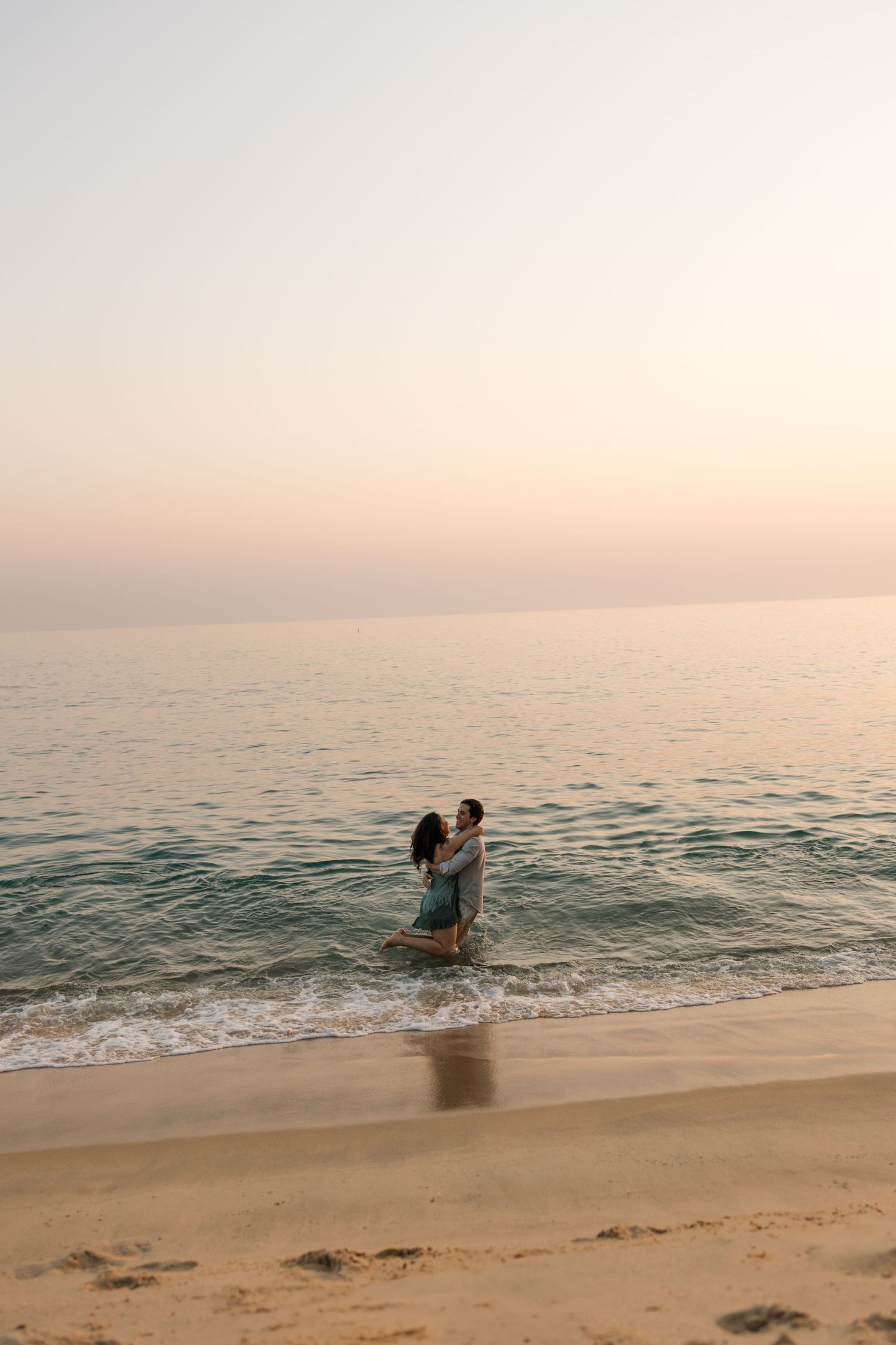 Silhouettes of beachgoers splashing and playing in shallow ocean water during golden hour.