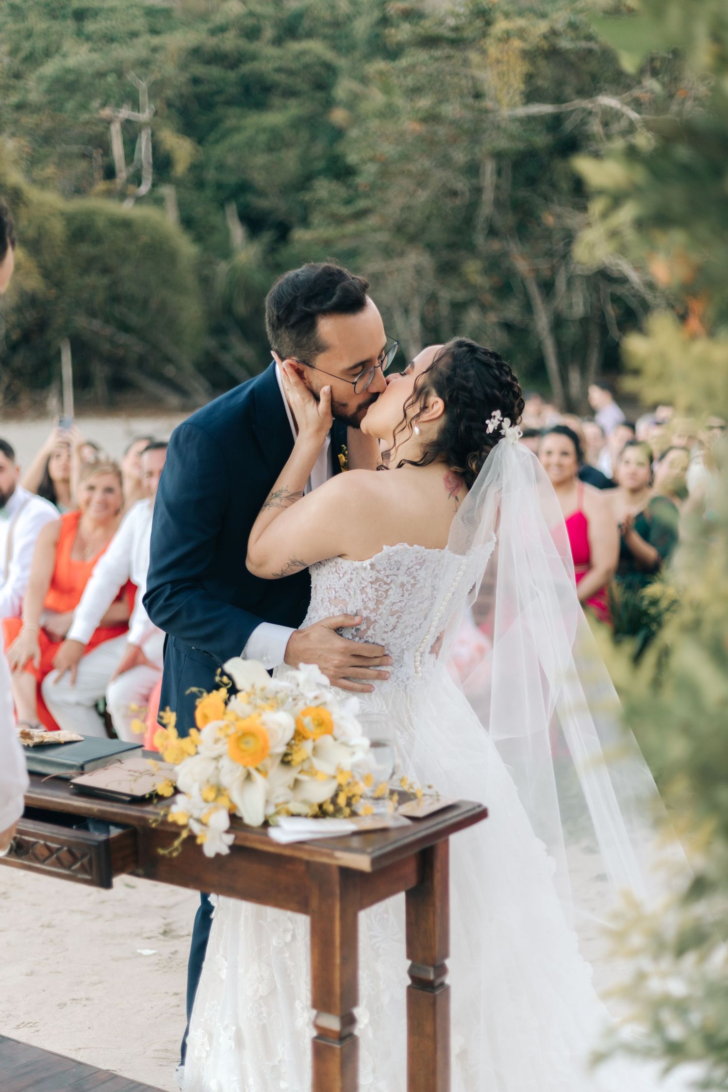 Newlyweds share their first kiss at altar decorated with yellow flowers.