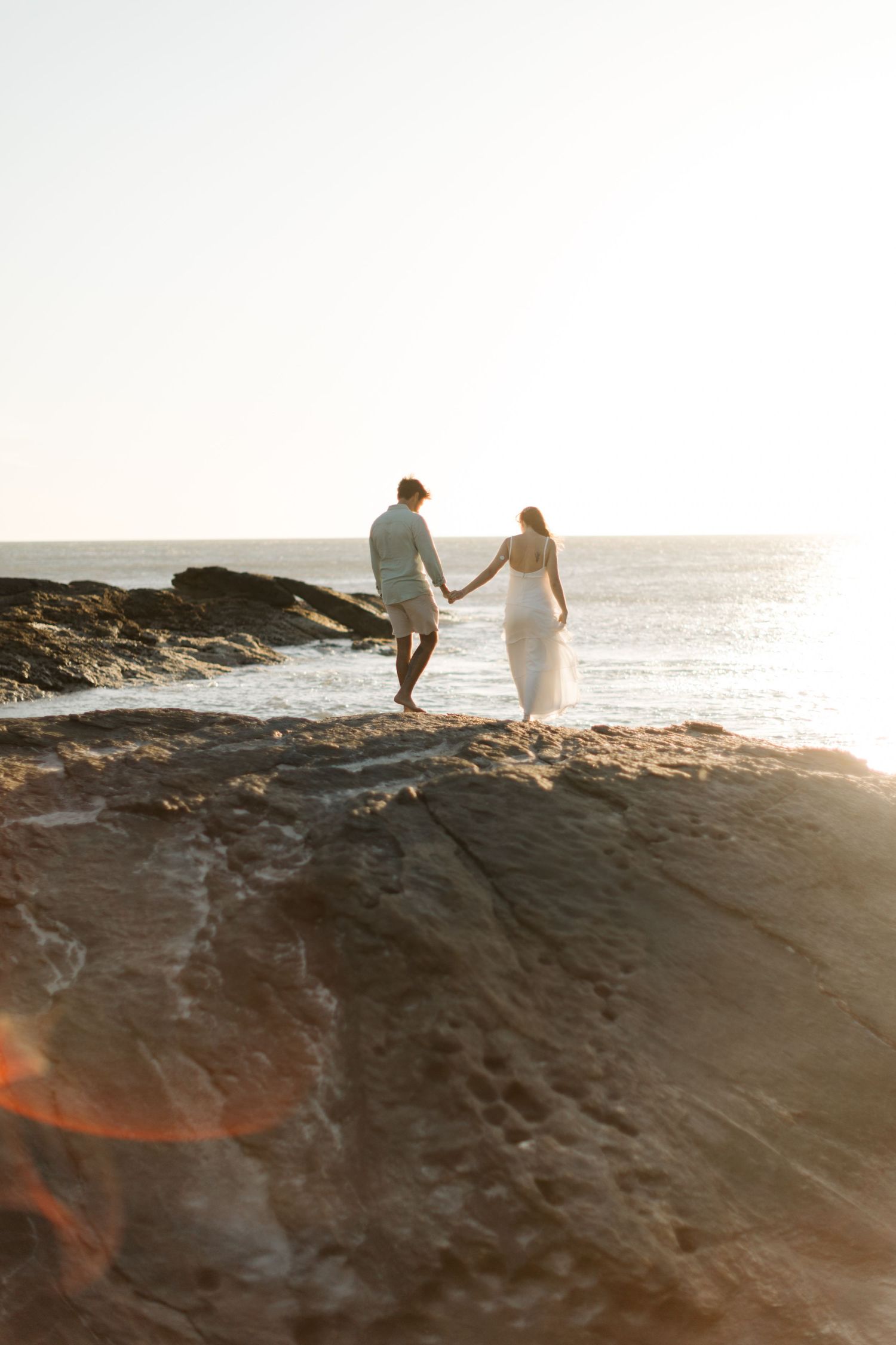 Silhouettes against a sunset sky walking along dramatic coastal rocks.