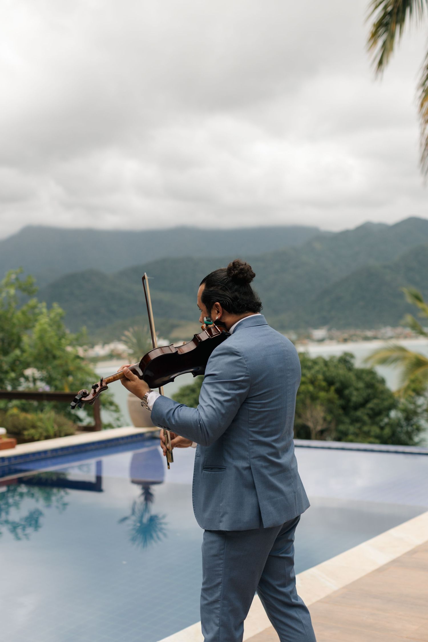 Person in light blue suit taking photos against mountain and infinity pool backdrop.