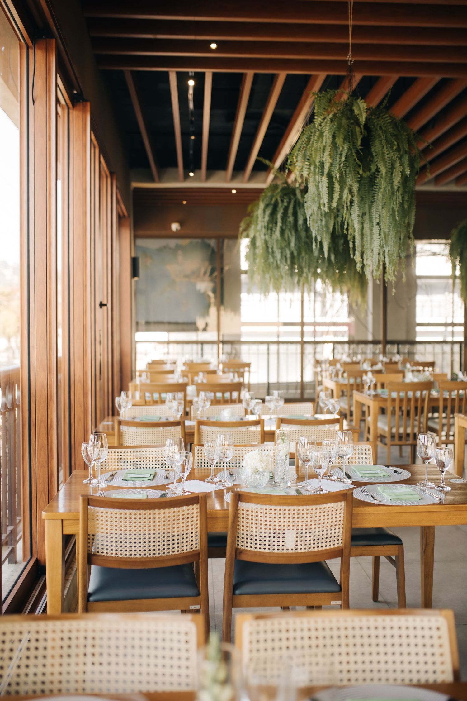 Modern wedding reception venue with cane back chairs and hanging plants under exposed wooden beams.