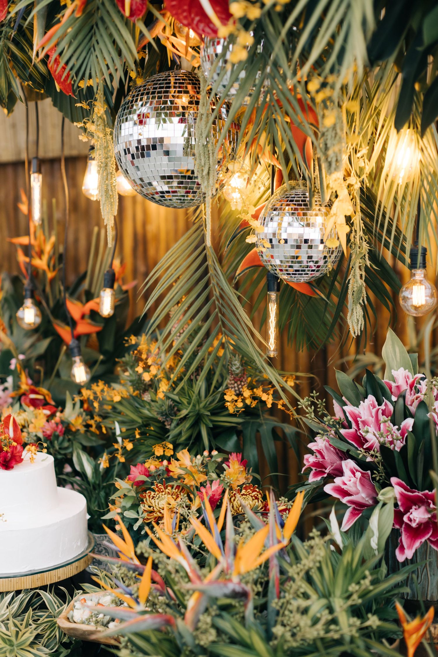Disco balls and tropical decor create a festive party atmosphere with palm fronds and pink lilies.