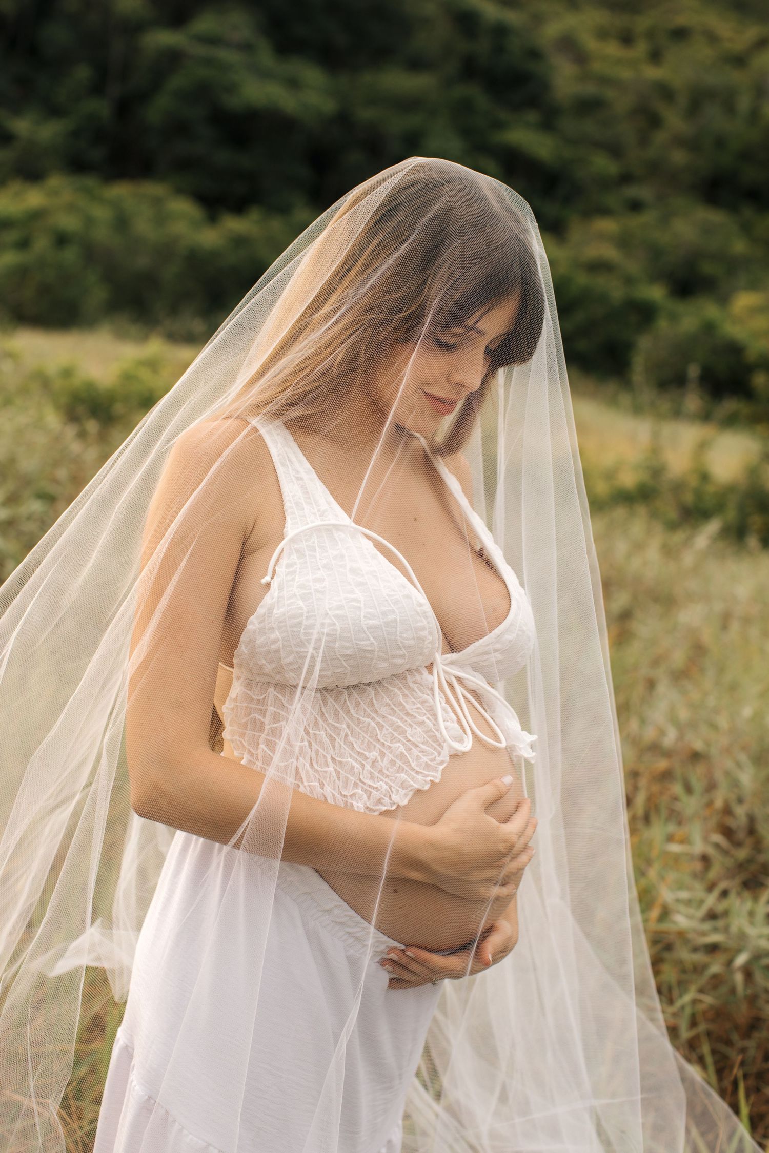 Woman in white lace dress with flowing veil poses gracefully in outdoor bridal portrait session.