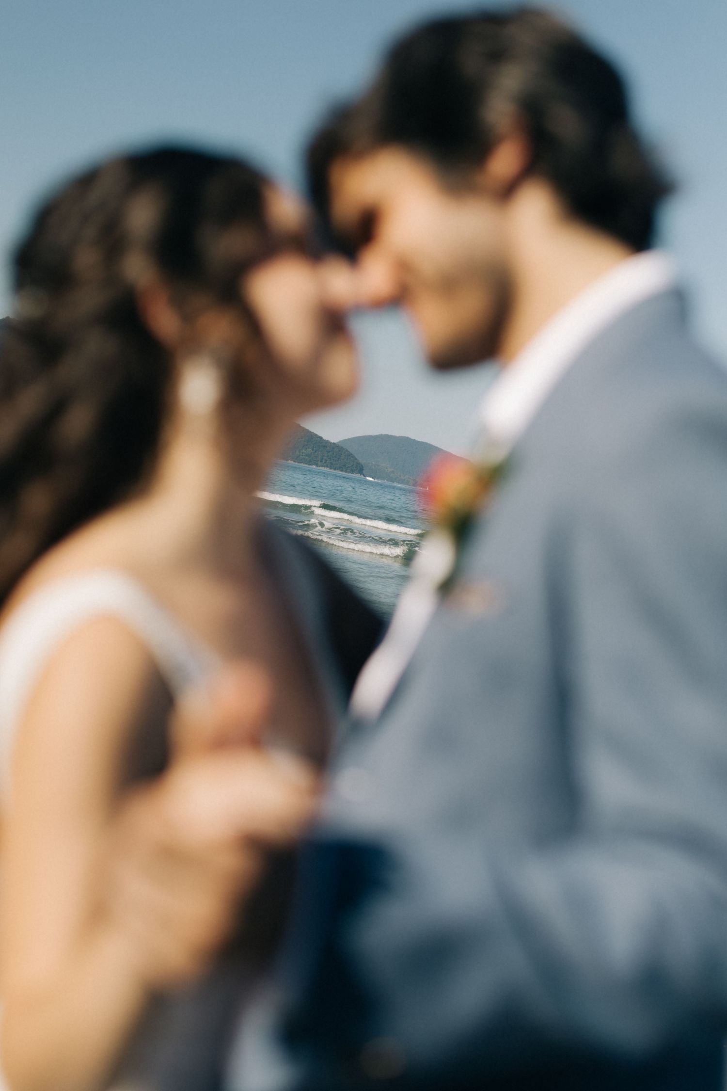 An intimate close-up wedding photo with ocean waves visible in the background.