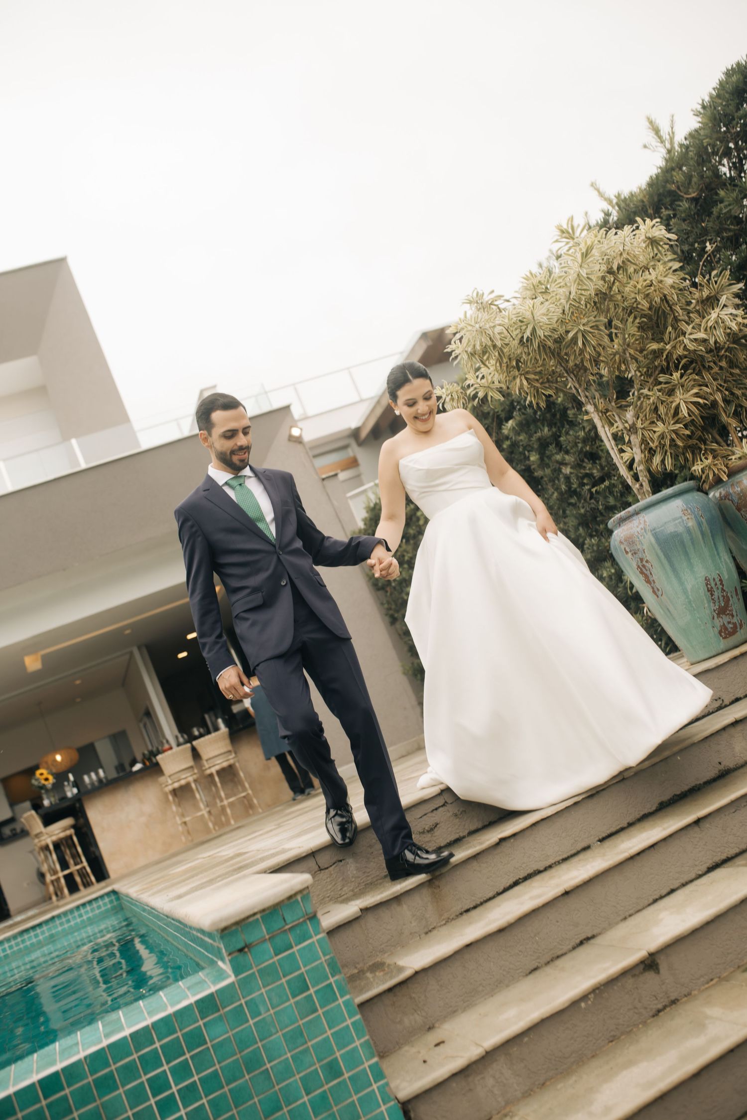 A newlywed couple descends turquoise-tiled steps outside a modern building.