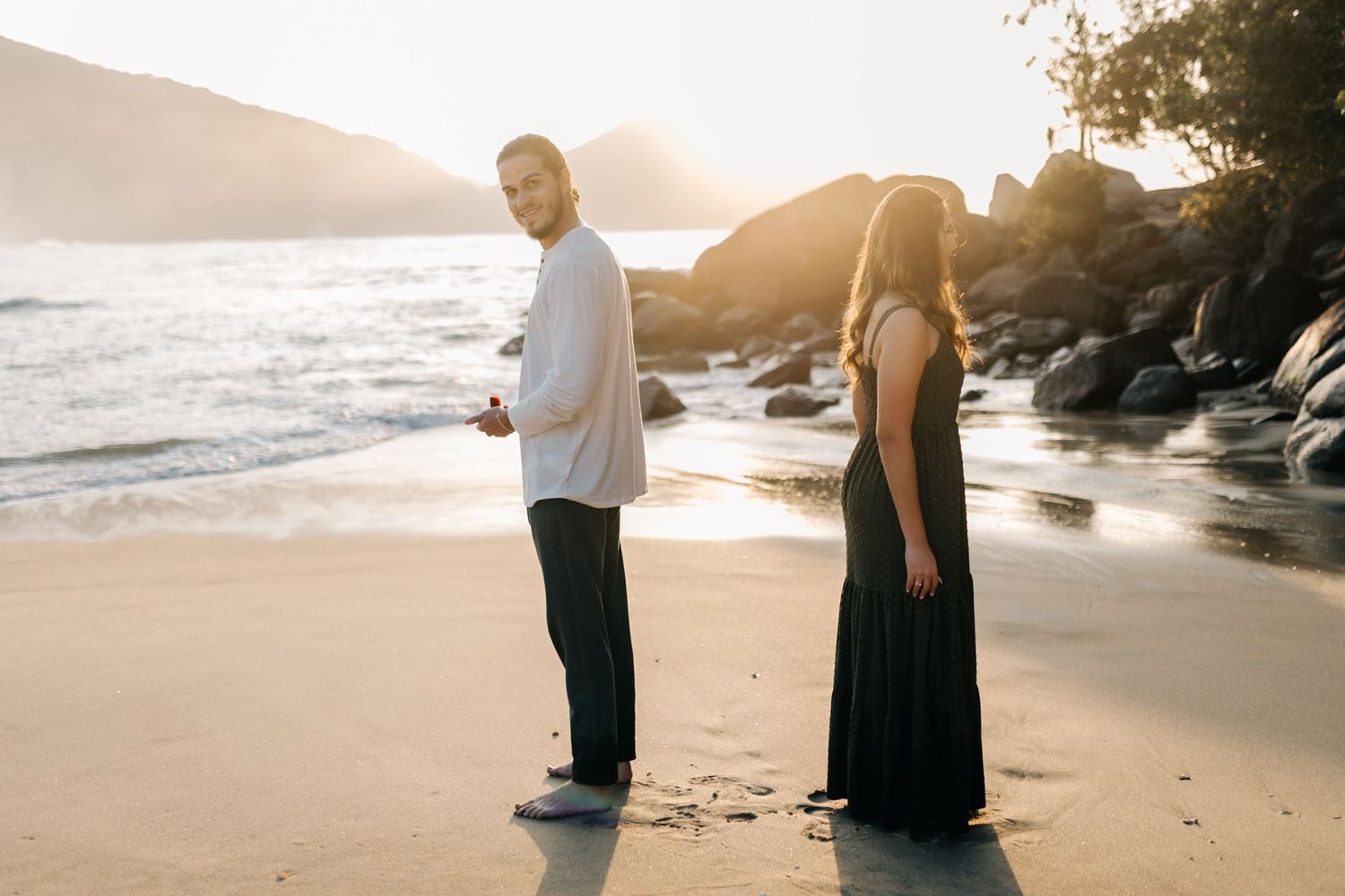 Side view of couple on beach examining footprints in sand during golden hour.