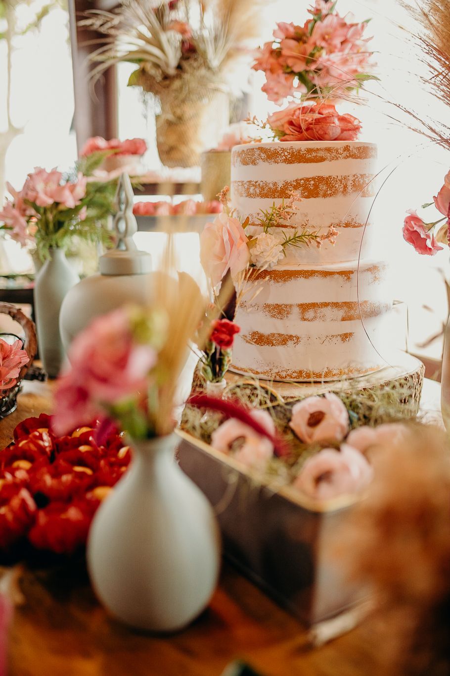 Elegant white tiered wedding cake decorated with pink flowers and floral arrangements.