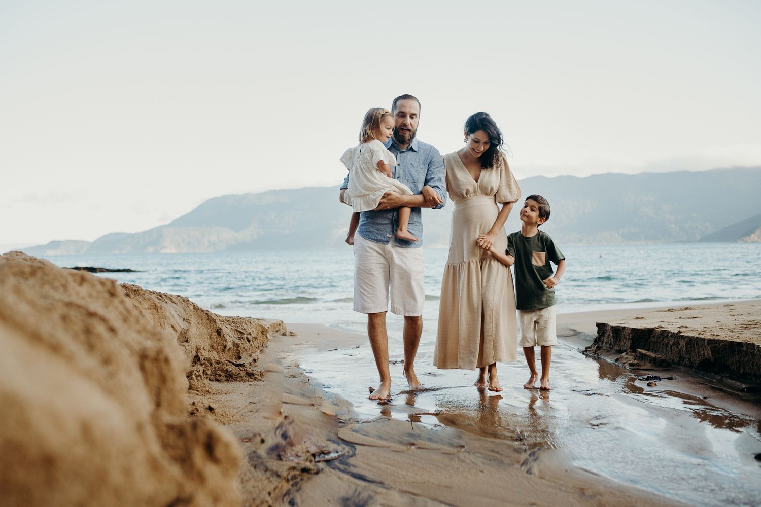 Family walking together on a rocky beach with mountains visible in the distance.