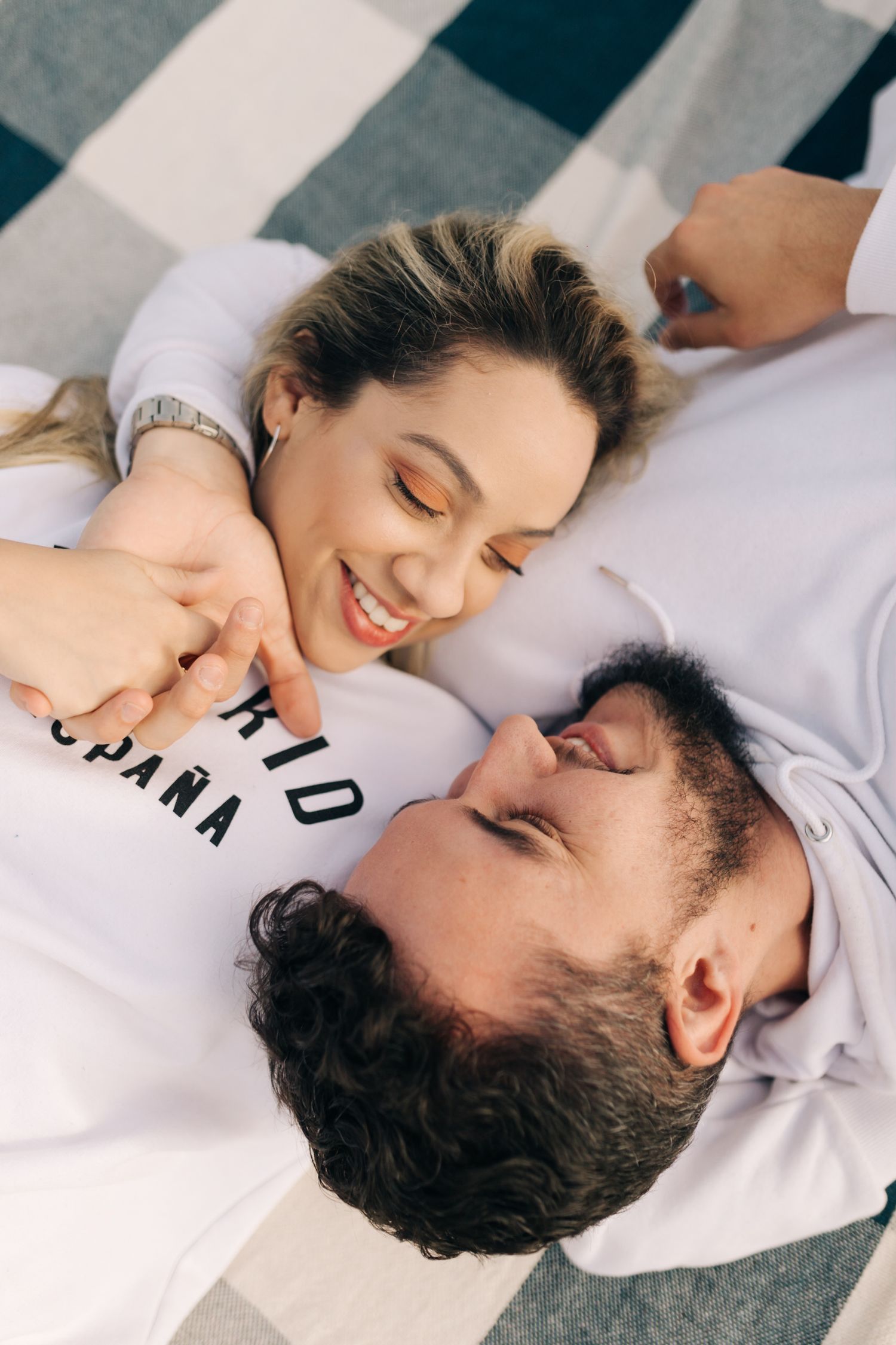 Close-up of happy couple resting on checkered blanket in white shirts.