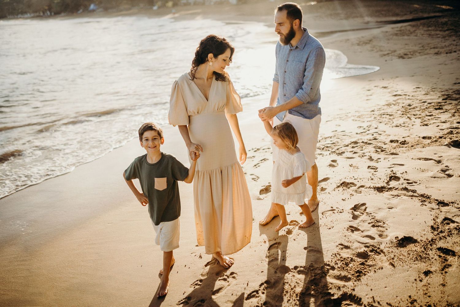 A family enjoys a casual walk together on a beach during golden hour.